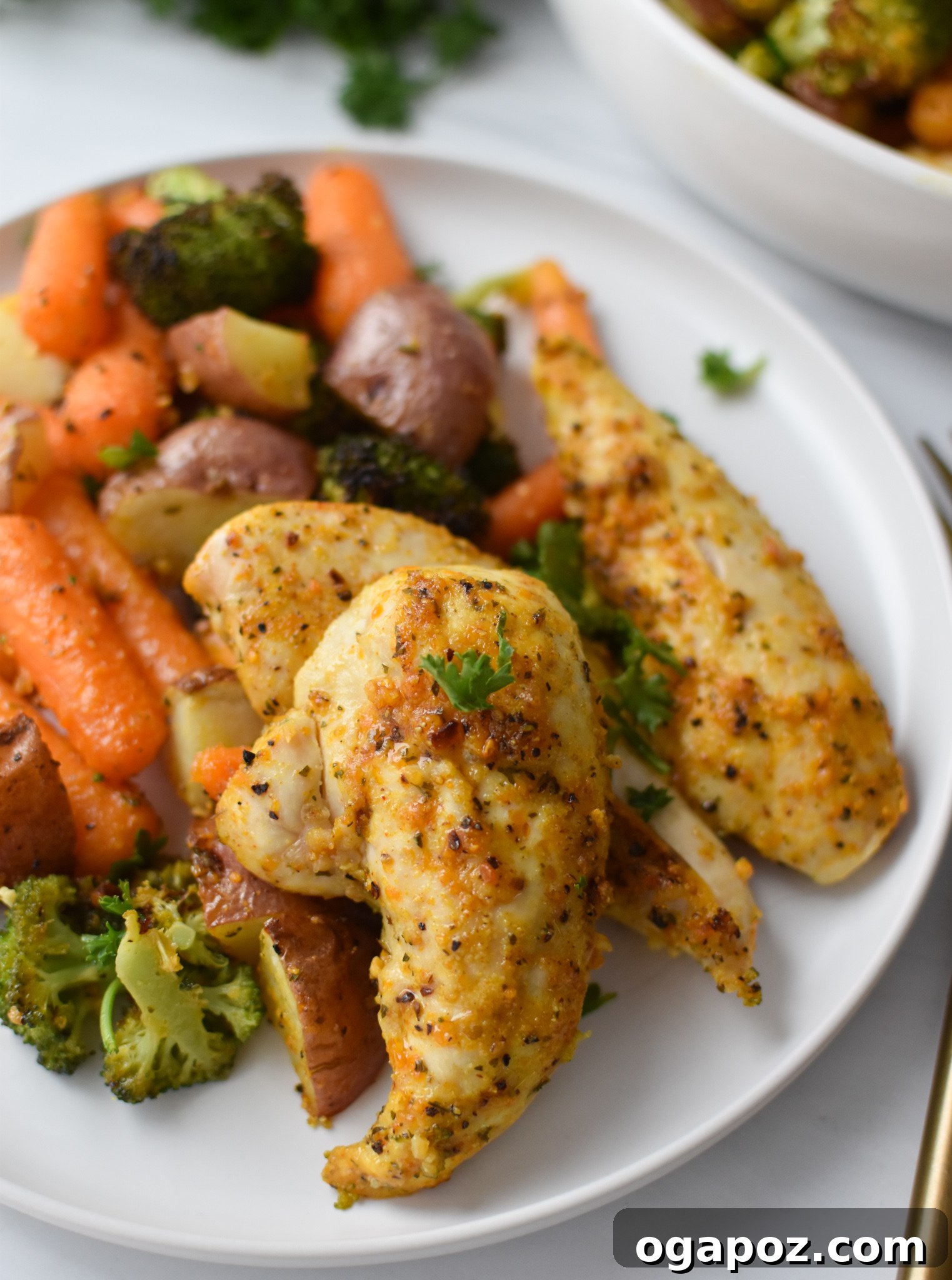 Tek Tepside Limonlu Parmesanlı Tavuk 11 A serving of Sheet Pan Lemon Parmesan Chicken Tenders with roasted vegetables on a white plate, garnished with fresh parsley.