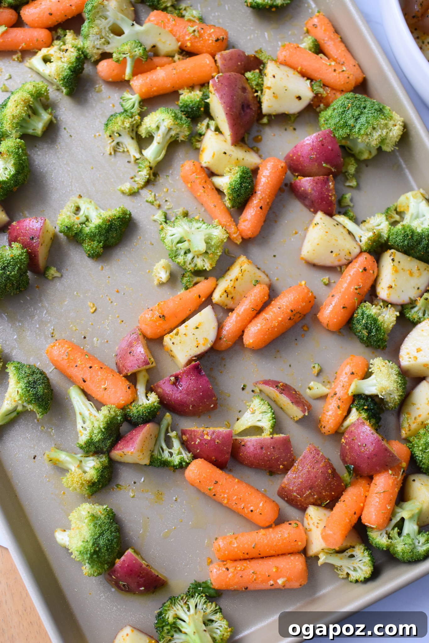 Tek Tepside Limonlu Parmesanlı Tavuk 7 Seasoned vegetables, including broccoli, carrots, and potatoes, spread in a single layer on a parchment-lined baking sheet.