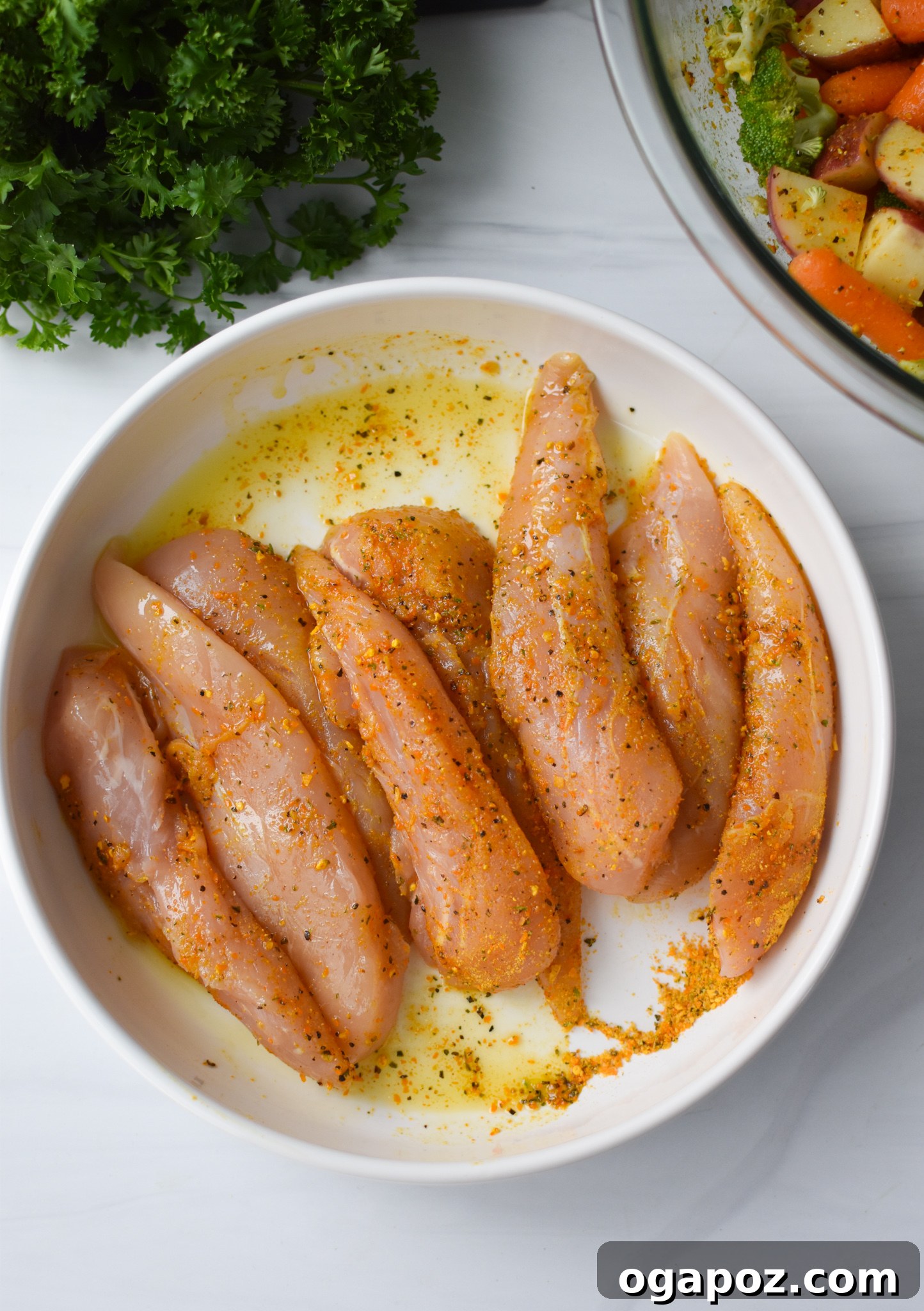 Tek Tepside Limonlu Parmesanlı Tavuk 8 Raw chicken tenderloins coated in lemon parmesan seasoning and olive oil in a mixing bowl.