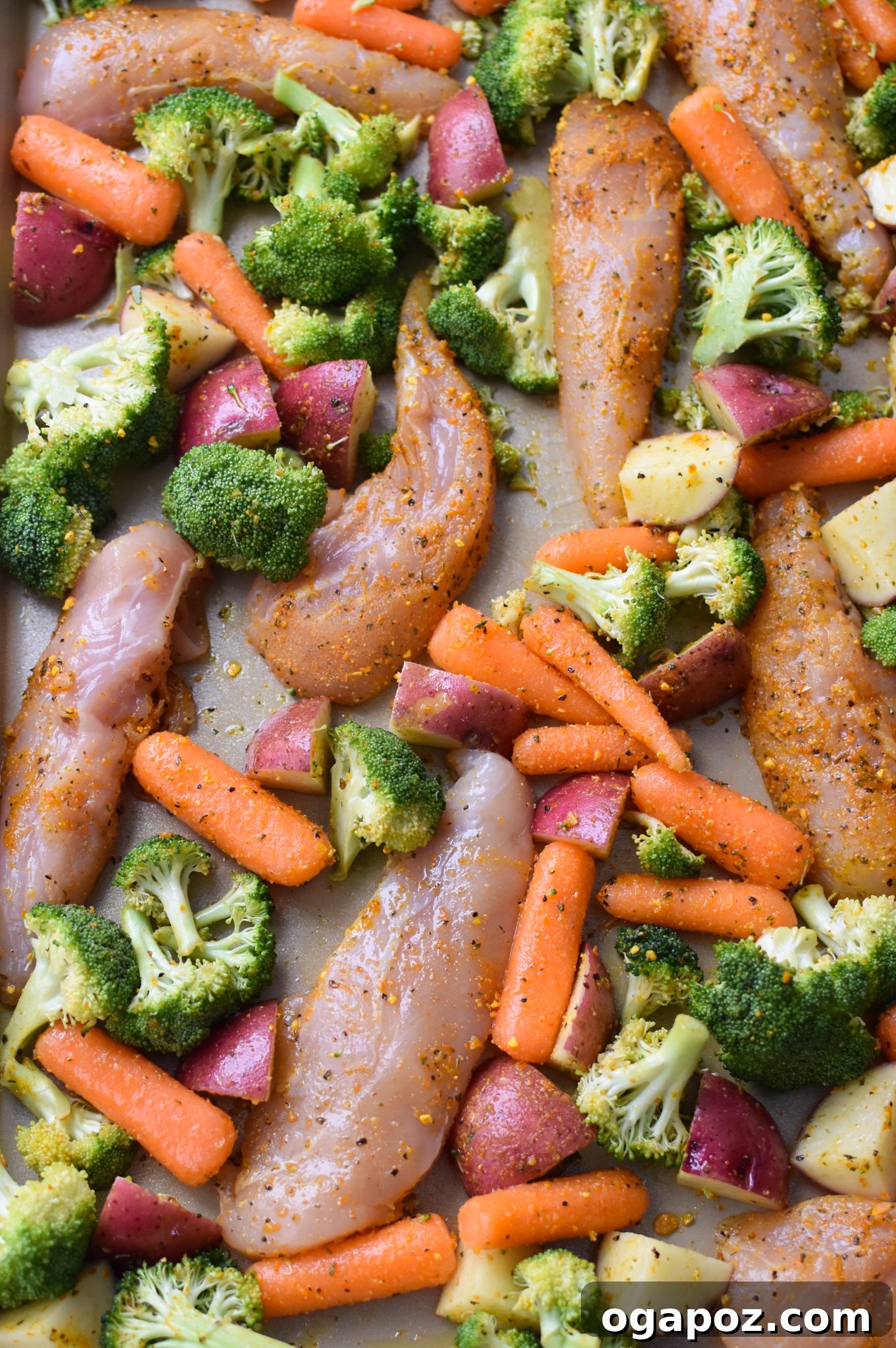 Tek Tepside Limonlu Parmesanlı Tavuk 9 Sheet pan with seasoned chicken tenderloins and vegetables (broccoli, carrots, potatoes) arranged in a single layer, ready for baking.