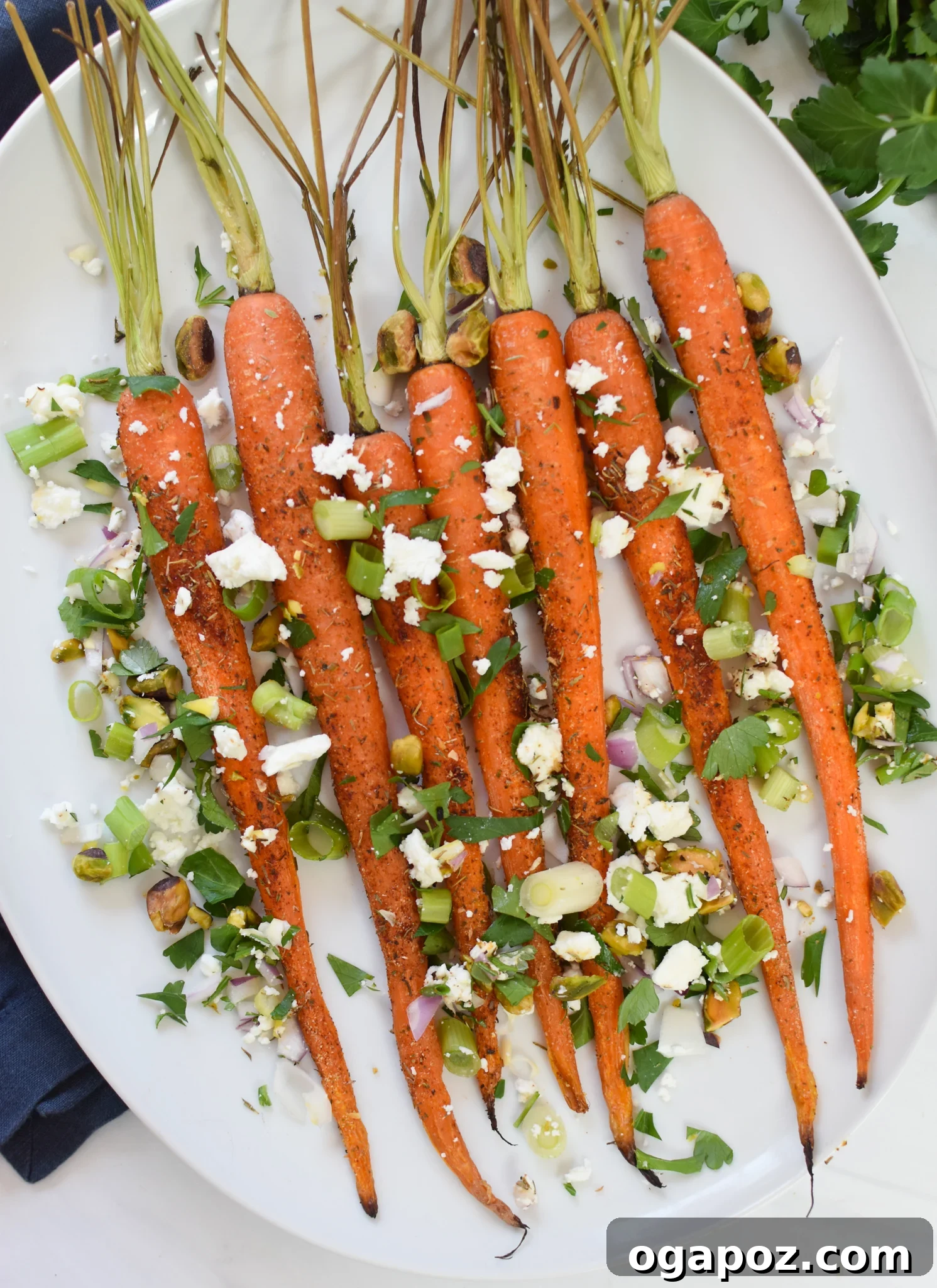 Golden Roasted Carrots with Crunchy Pistachios 2 Roasted Carrots with Pistachios on a white platter, garnished with fresh herbs and feta.