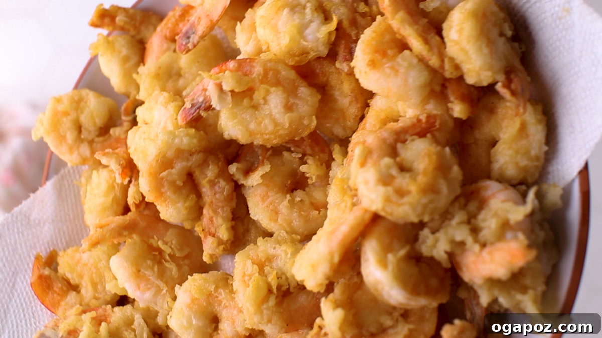 Crispy Fried Cooked Shrimp 8 Freshly fried cooked shrimp draining on a paper towel-lined plate.