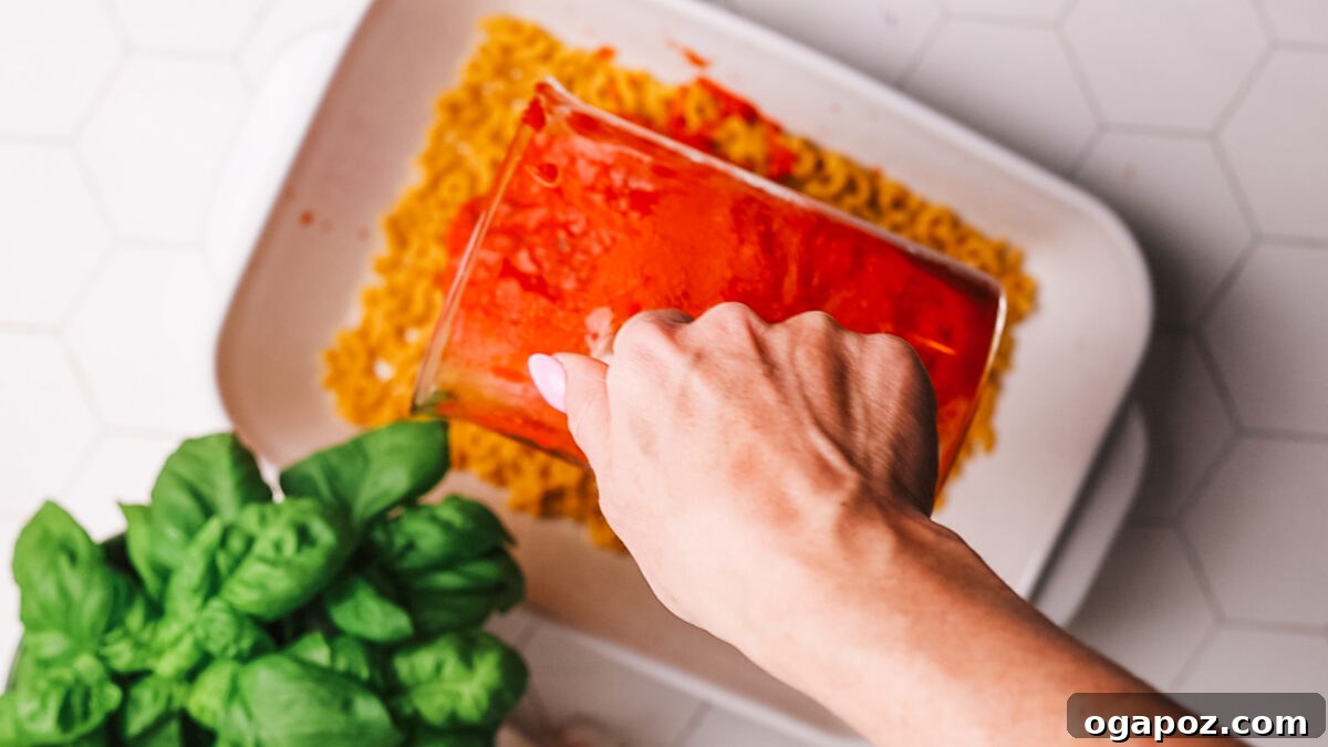 Cheeseburger Casserole 5 Pouring marinara sauce over uncooked pasta.