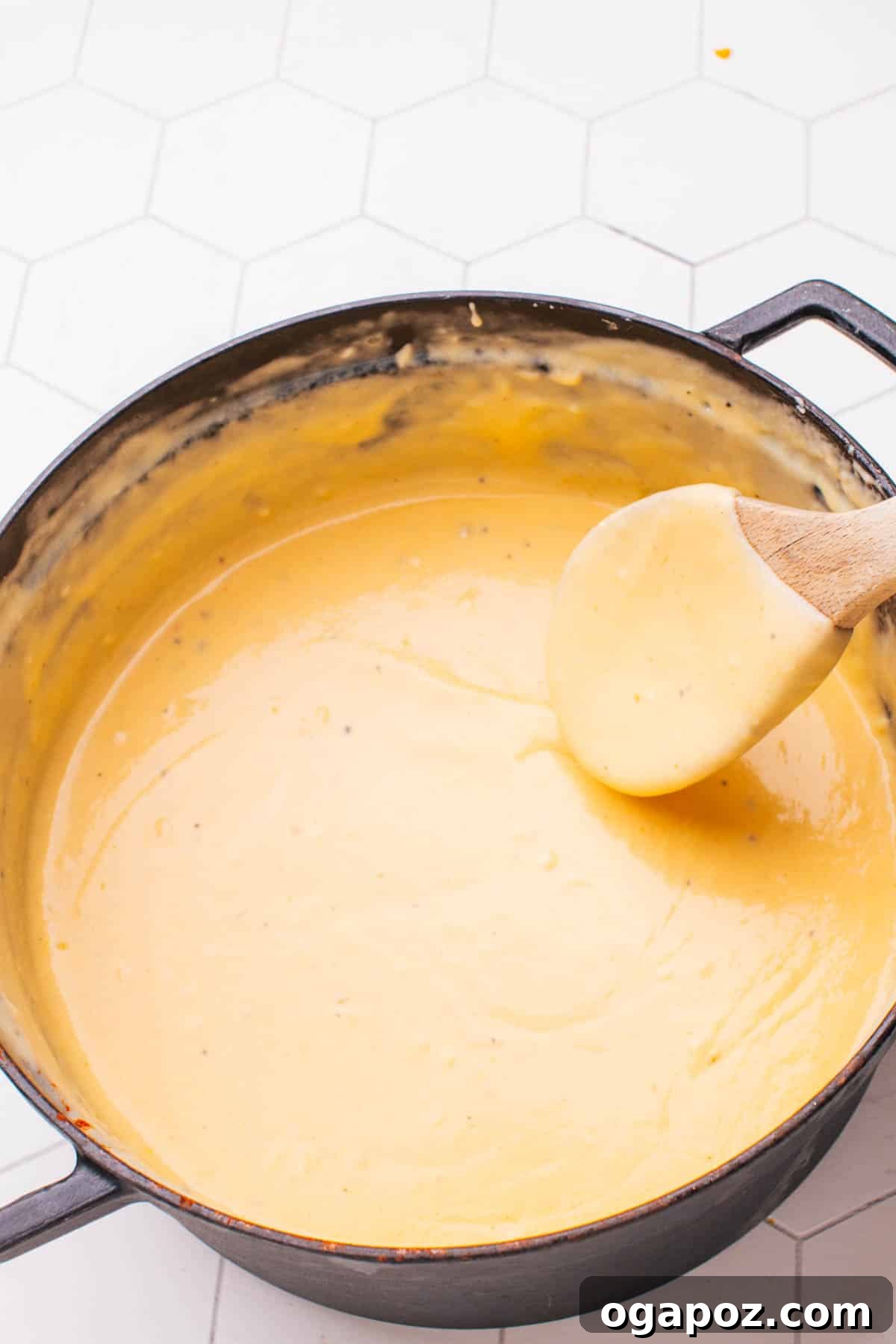 Steamed cauliflower florets being gently folded into a rich and creamy cheese sauce in a large mixing bowl.