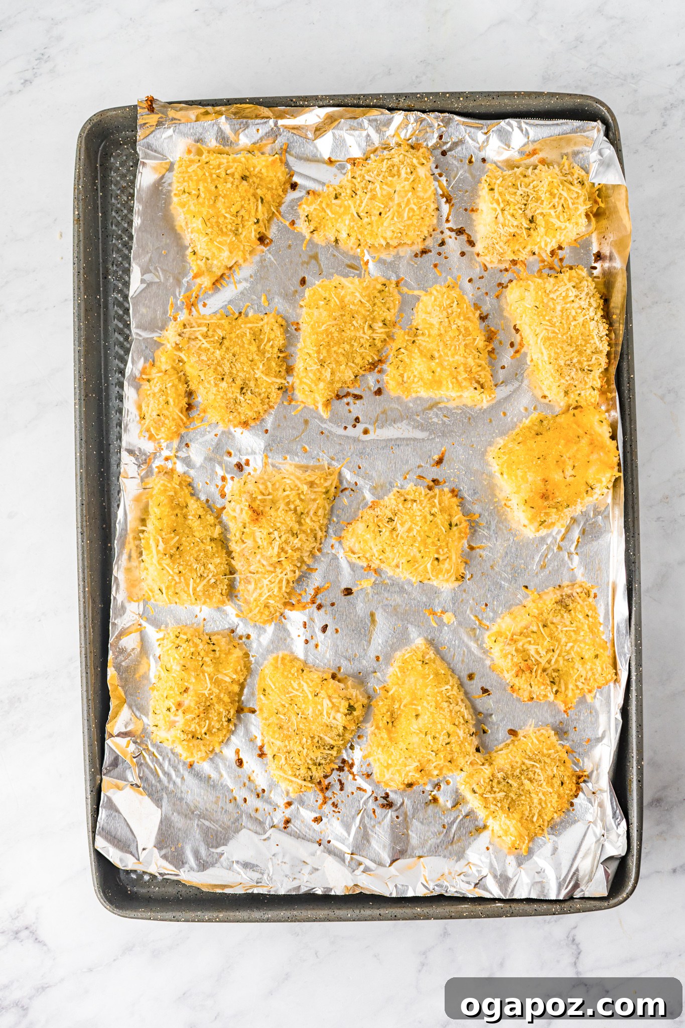 Breading-coated tilapia fish sticks arranged on a baking sheet.