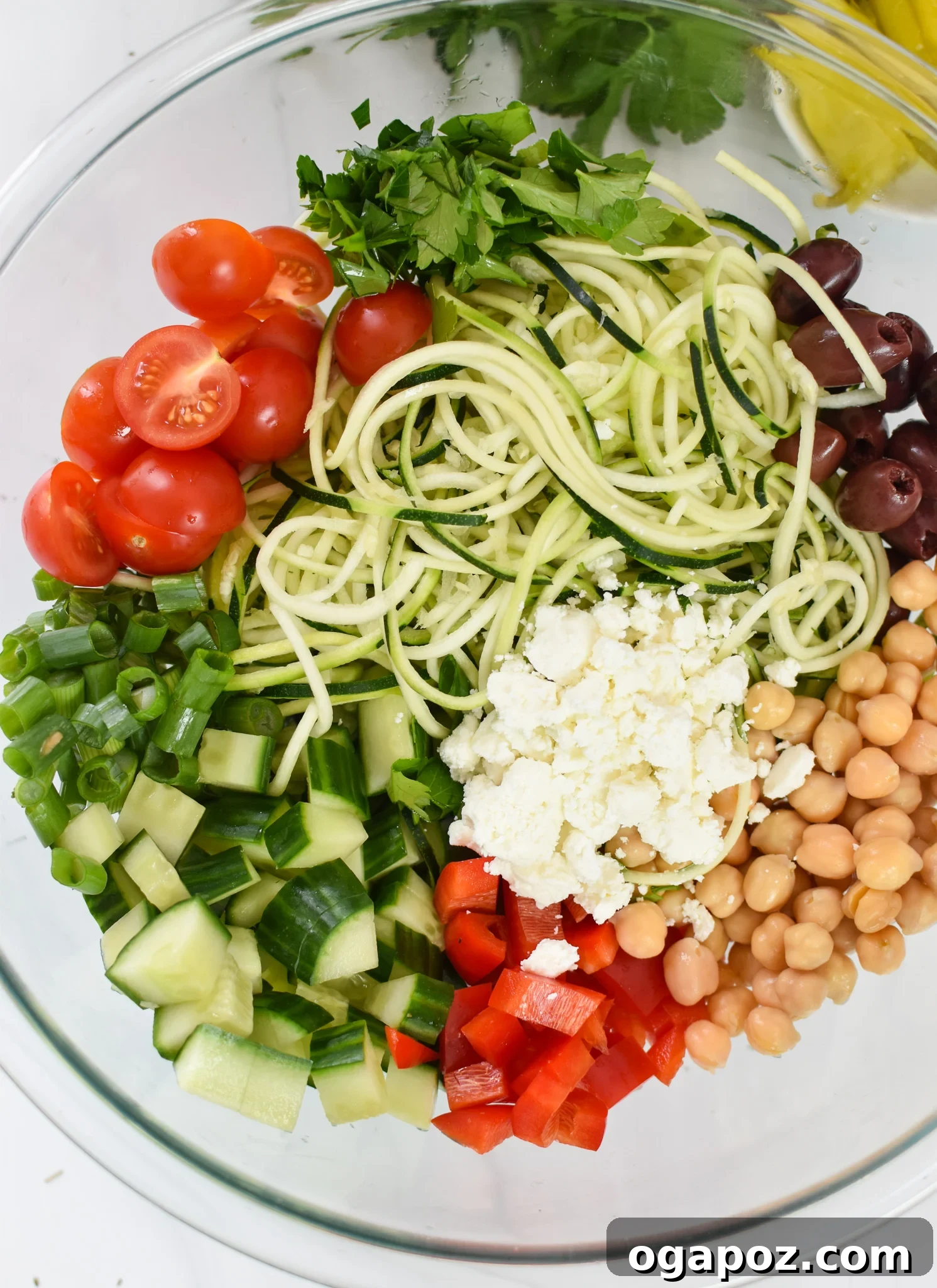 Vibrant Mediterranean Zucchini Pasta Salad 4 A close-up shot of the mixed Mediterranean Zucchini Pasta Salad ingredients in a glass bowl before dressing, showcasing the vibrant colors and textures.