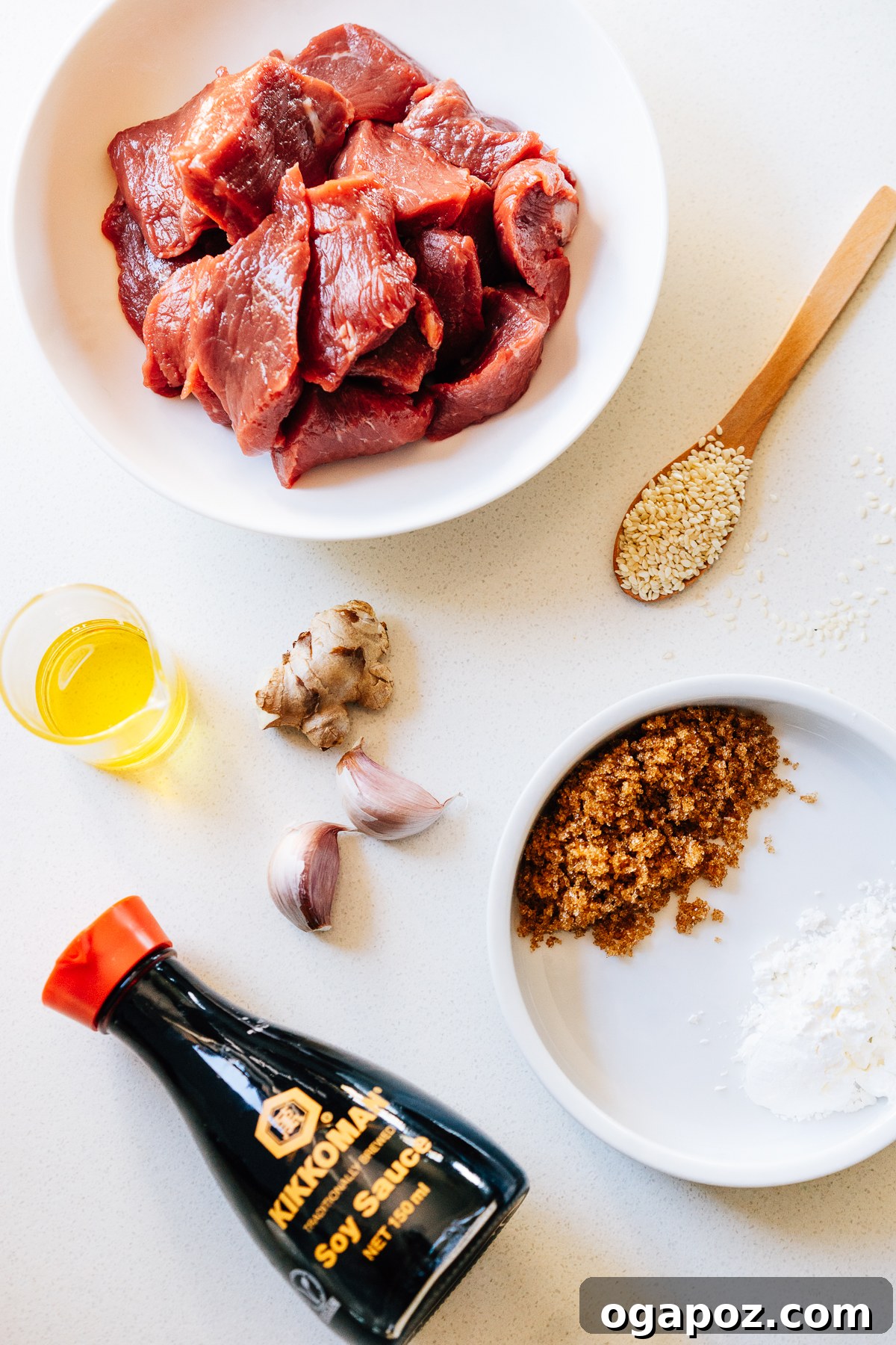 A flat lay photograph showcasing all the ingredients required for making Beef Teriyaki, including soy sauce, brown sugar, cornstarch, garlic, ginger, flank steak, neutral oil, green onions, and sesame seeds.