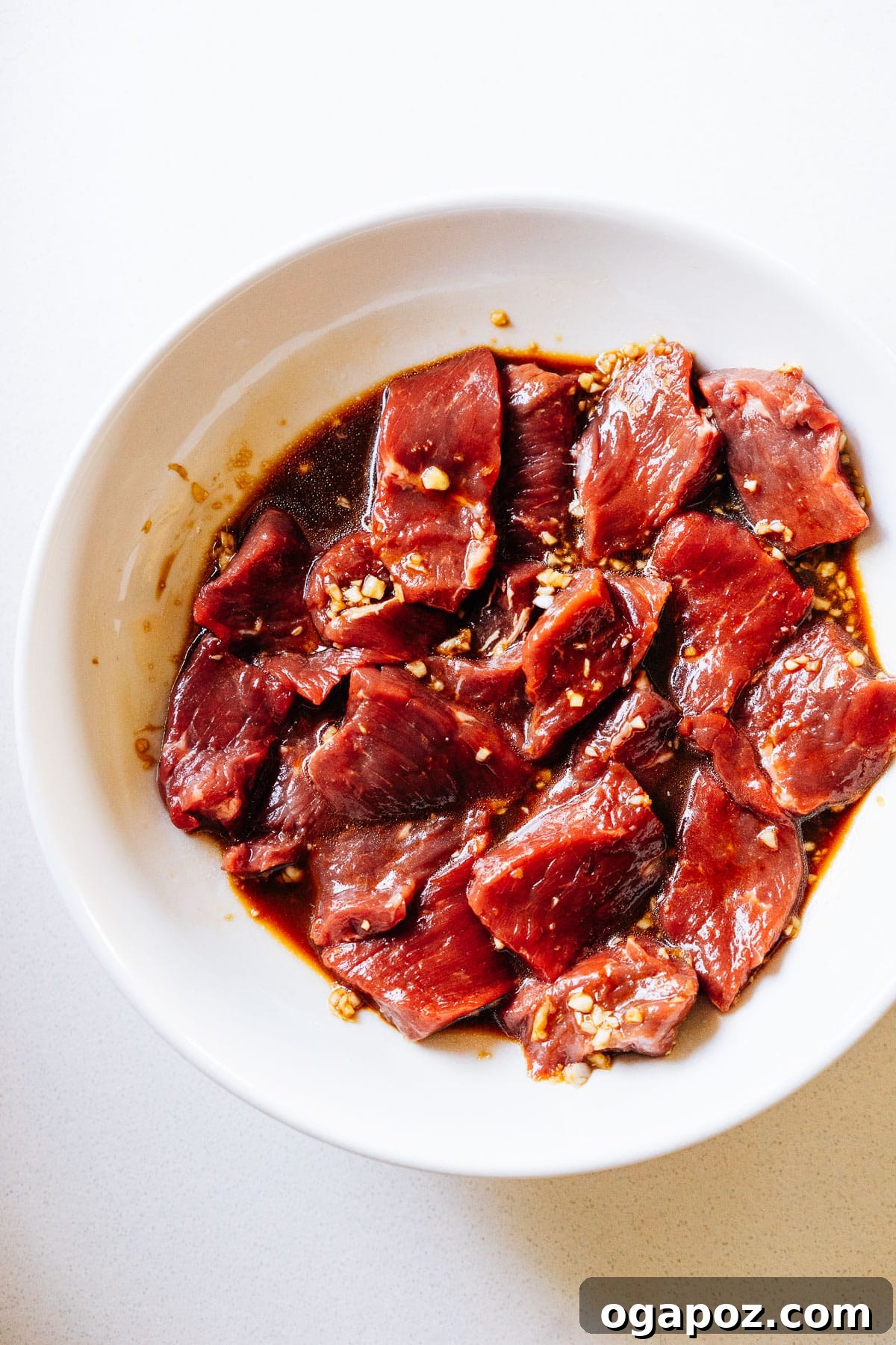 Thinly sliced beef being tossed and coated in a flavorful teriyaki marinade within a bowl.
