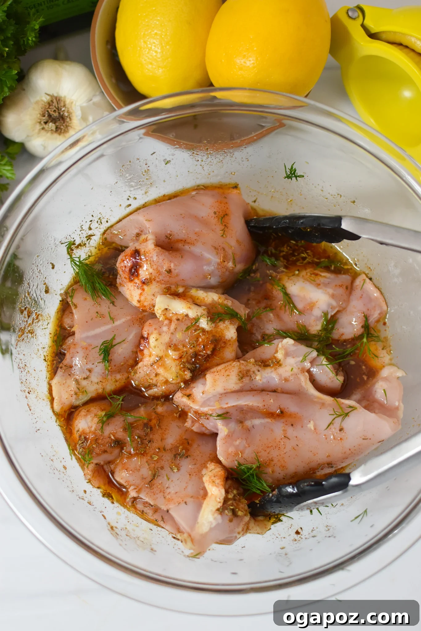 Chicken thighs marinating in a clear glass bowl, soaking up Greek flavors.