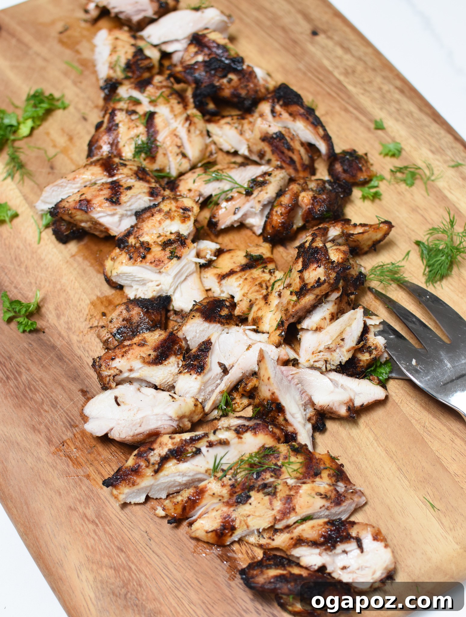 Sliced grilled Greek chicken on a cutting board, ready for the salad.
