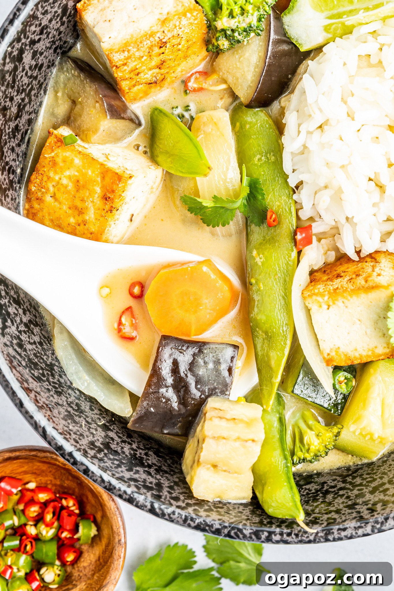 Quick & Delicious Thai Veggie Green Curry 4 A close-up of a spoon scooping a generous portion of Thai Vegetable Green Curry from a bowl, highlighting its rich, creamy texture and colorful cooked vegetables.