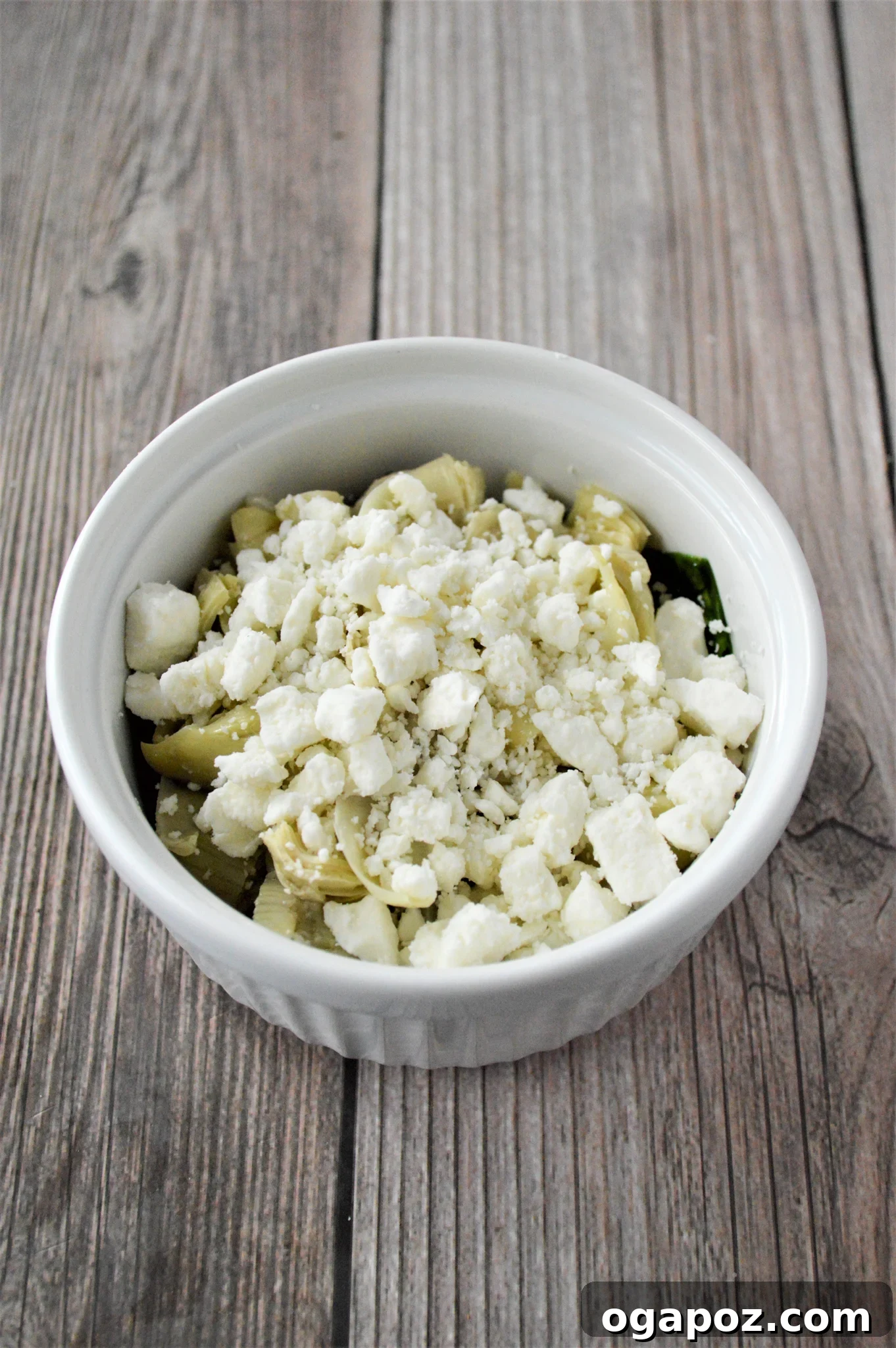 Rustic Greek Egg Bake 8 Feta cheese crumbled over artichokes in a ramekin for Greek Baked Eggs.