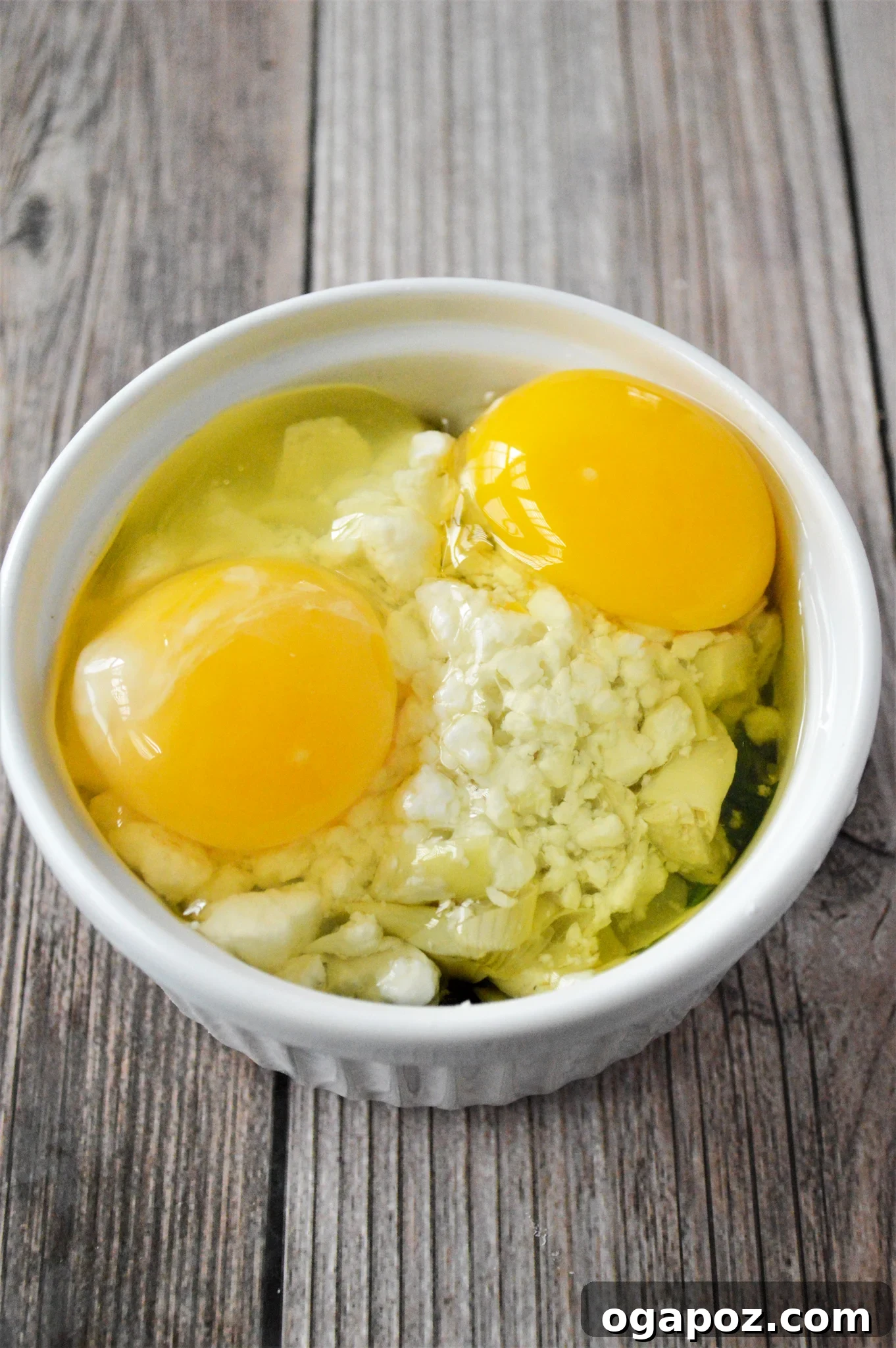 Rustic Greek Egg Bake 9 Two eggs cracked on top of feta cheese in a ramekin.