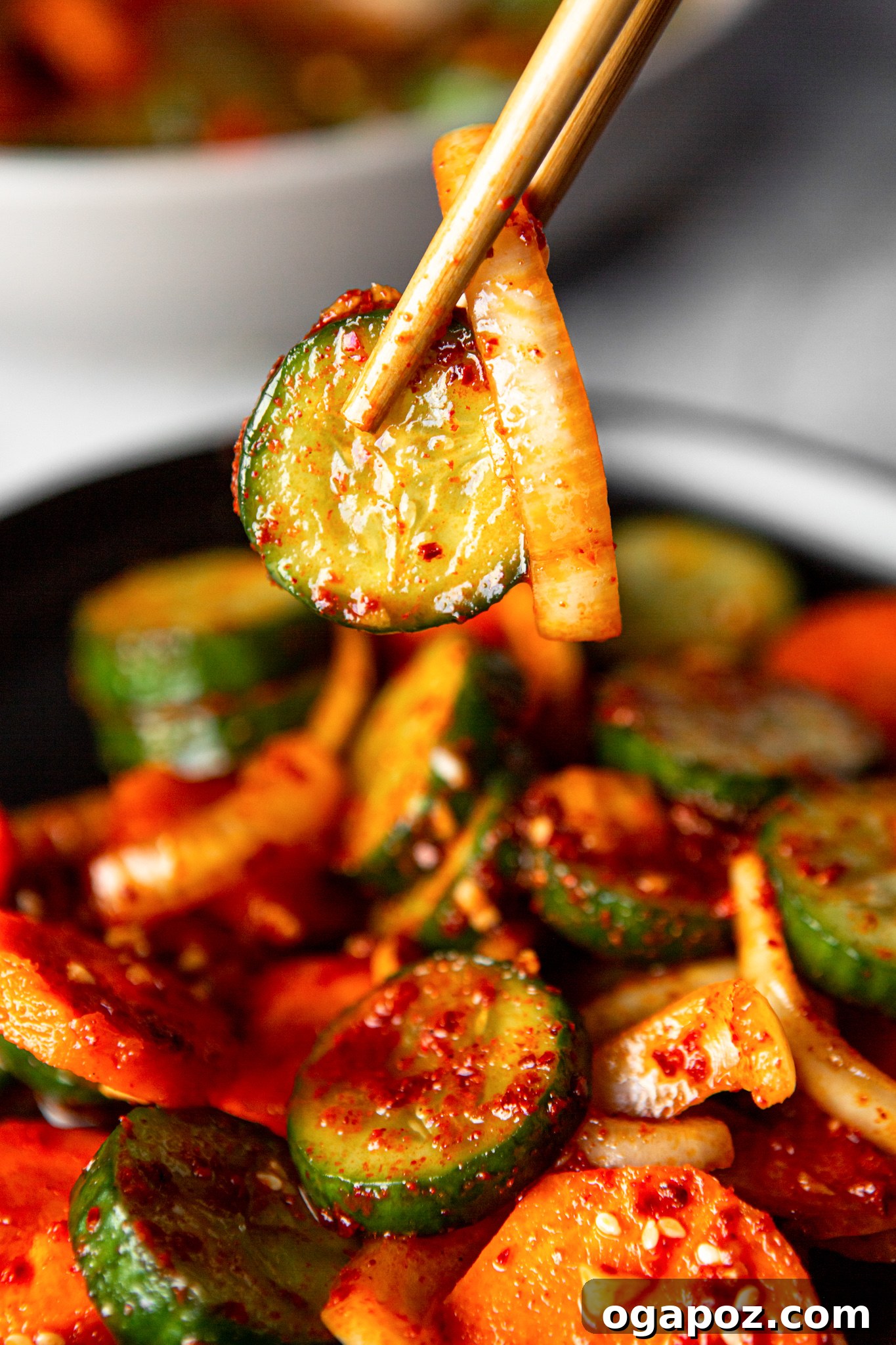 Instant Cucumber Kimchi 3 Close-up of Quick Korean Cucumber Kimchi with wooden chopsticks poised to pick up a piece, emphasizing its vibrant colors and crisp texture.