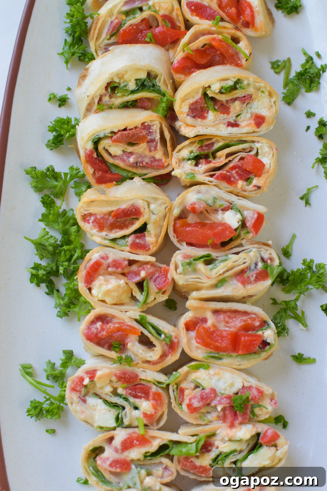 A close-up of finished Mediterranean Pinwheels, elegantly arranged on a serving platter with fresh parsley garnish.