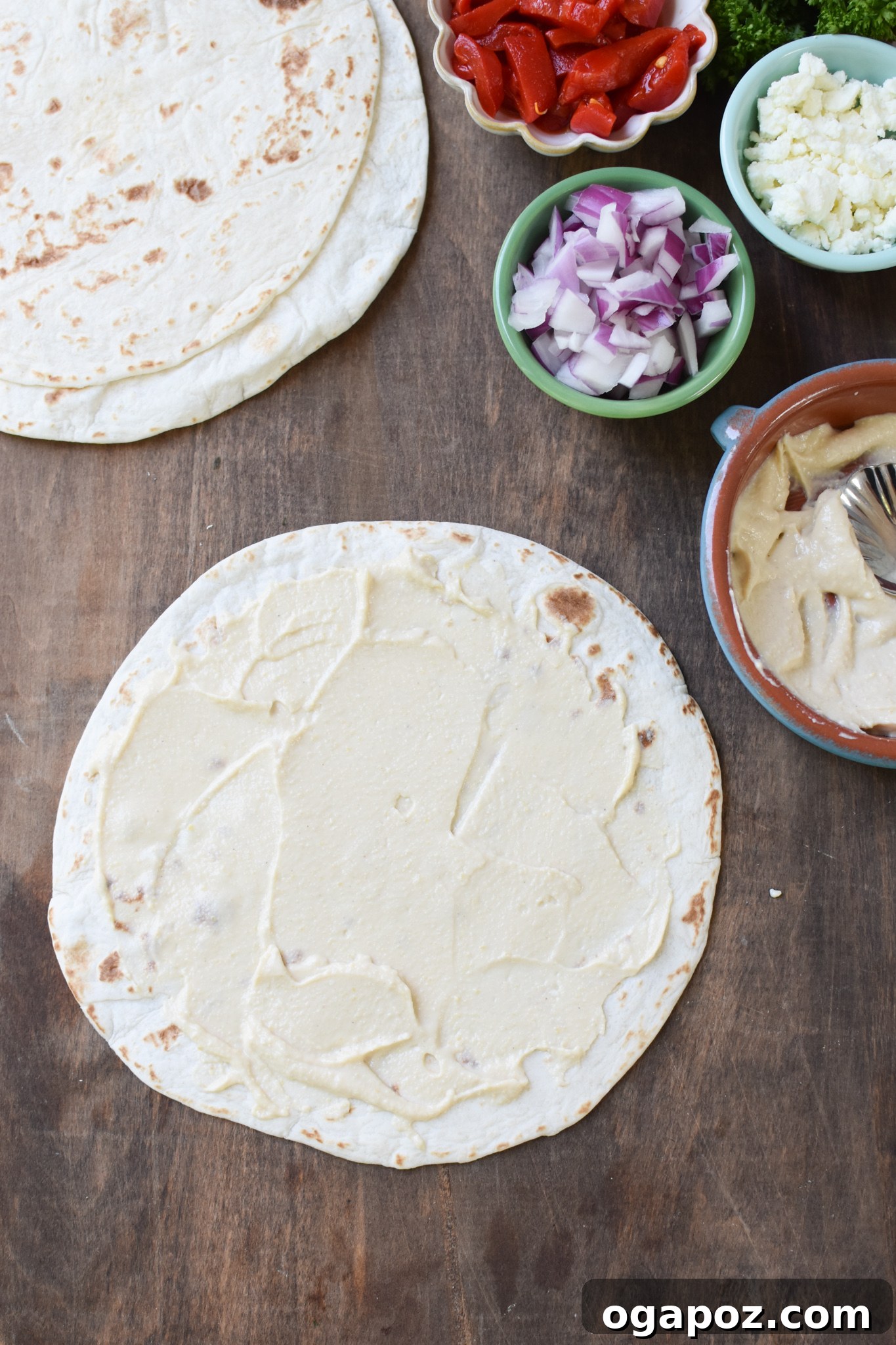 A large tortilla spread evenly with a layer of creamy hummus, ready for the next ingredients.