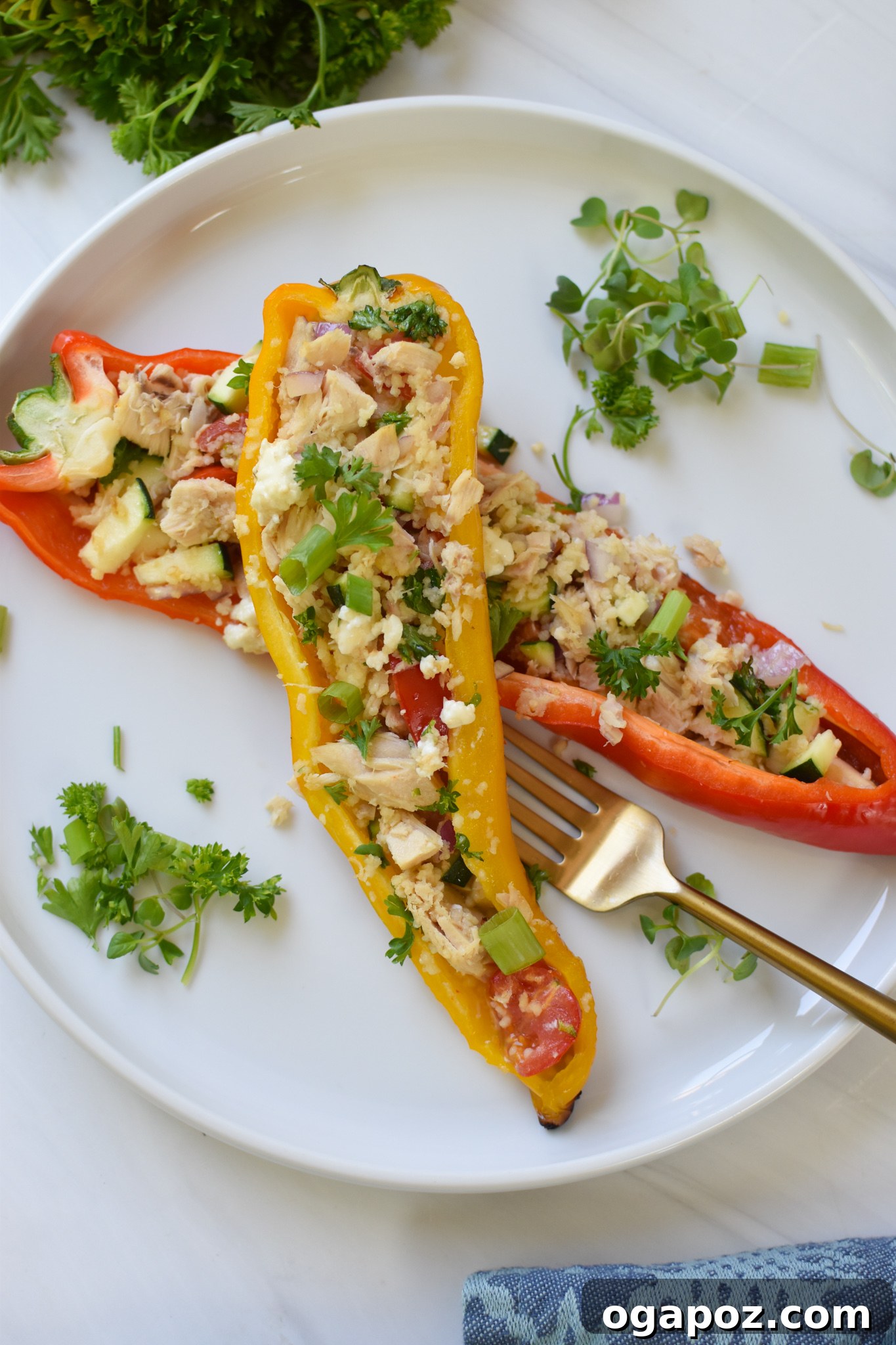 Sun-Kissed Mediterranean Tuna Couscous Peppers 3 Mediterranean Tuna Couscous Stuffed Peppers on a white plate with a gold fork, ready to be enjoyed.