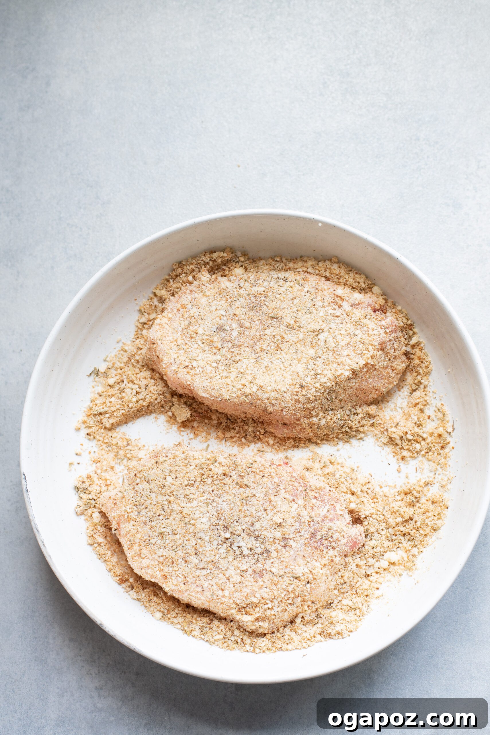 Crispy Parmesan Pork Chops 6 Close-up of a Parmesan crusted pork chop in a bowl of breadcrumbs, showing the coating process.