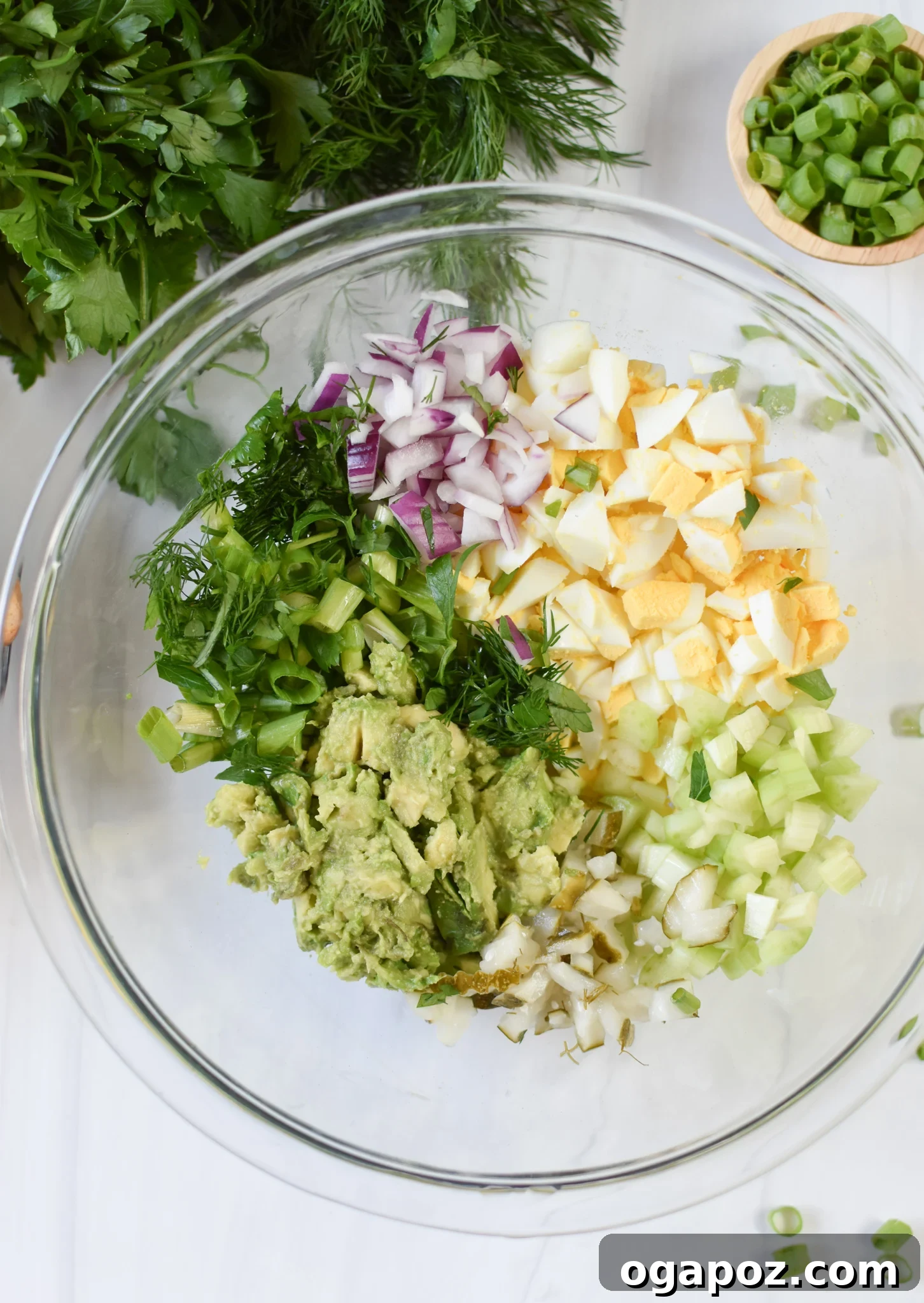 Green Goddess Egg Salad 5 Avocado Egg Salad ingredients being mixed in a bowl, showing fresh produce and creamy avocado.