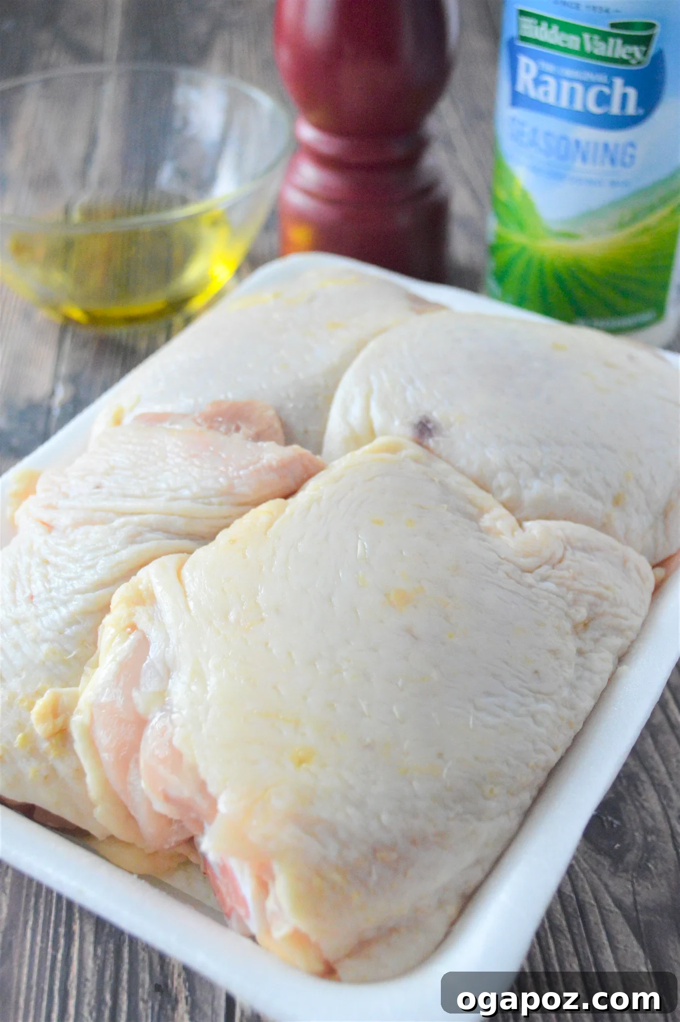 Creamy Ranch Chicken Thighs 5 Raw chicken thighs coated in olive oil inside a glass baking dish, ready for seasoning application.