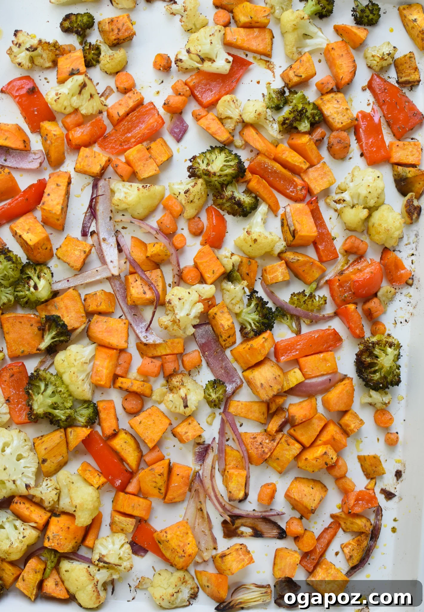 Wholesome Sweet Potato Bowl 6 Sweet potatoes and various vegetables spread evenly on a parchment-lined baking sheet, roasting in the oven to tender perfection.