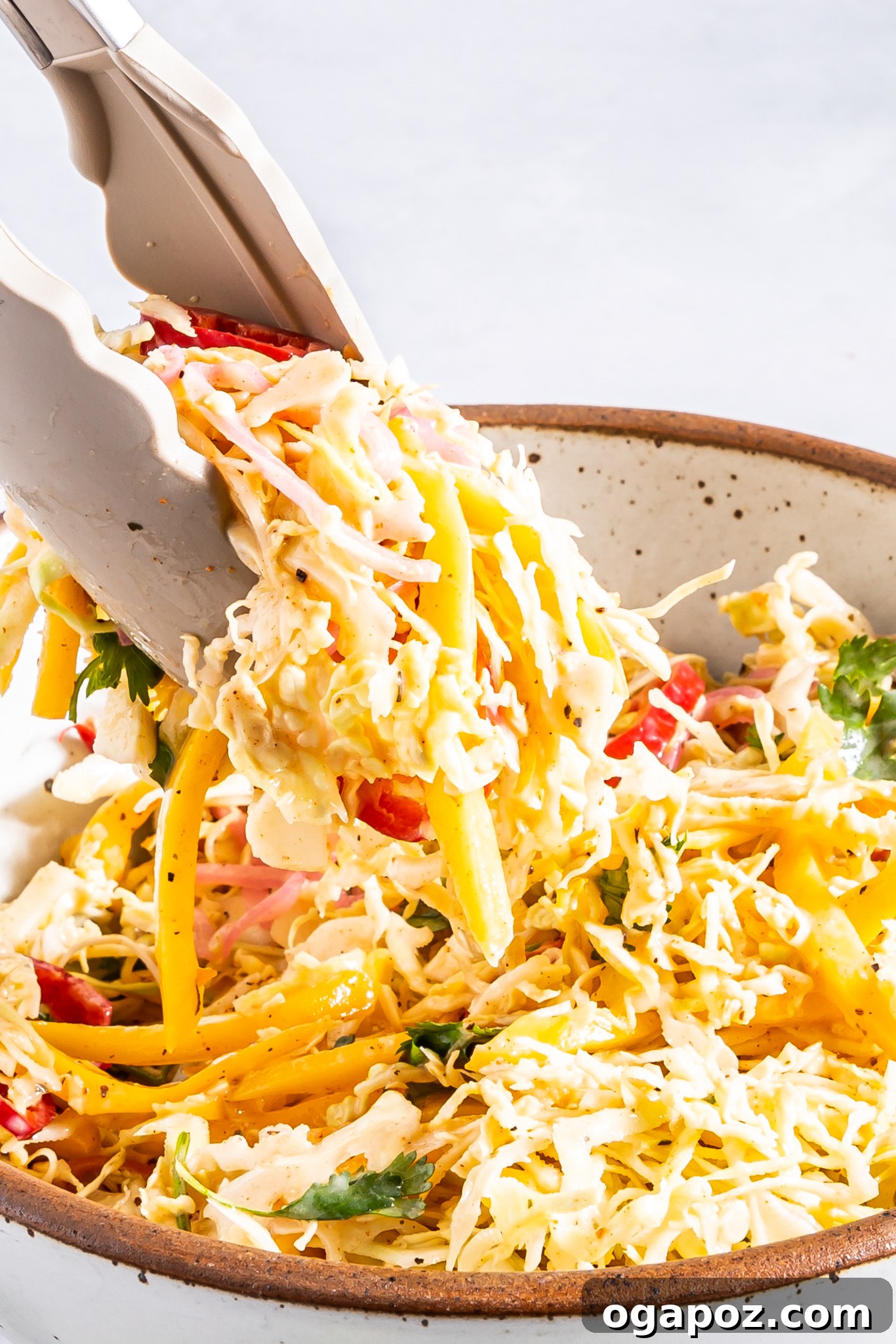 Easy Caribbean Coleslaw Recipe being tossed with tongs in a large bowl.