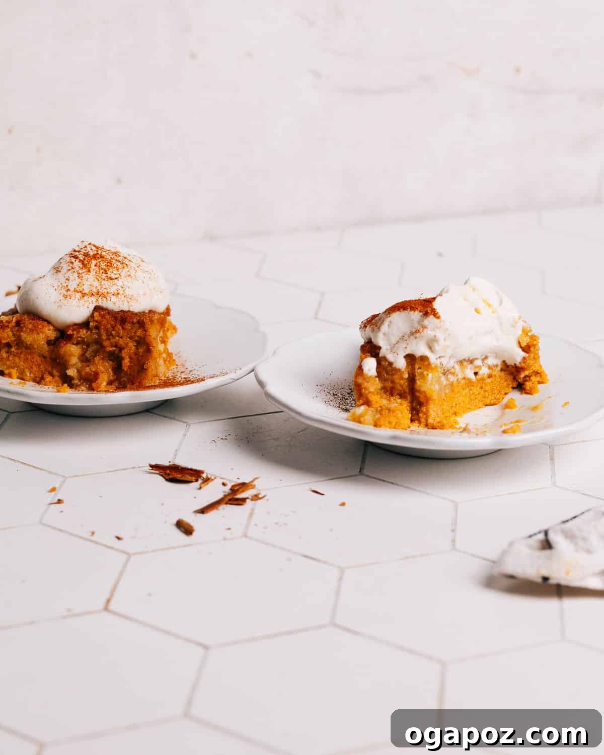 Two plates of Pumpkin Dump Cake, each topped with a generous dollop of whipped cream, artfully arranged on a rustic table.