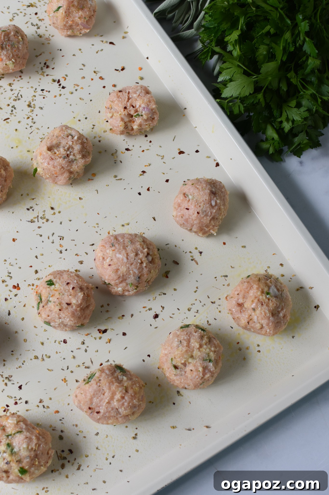Uncooked baked chicken meatballs arranged on a baking sheet, ready for the oven.