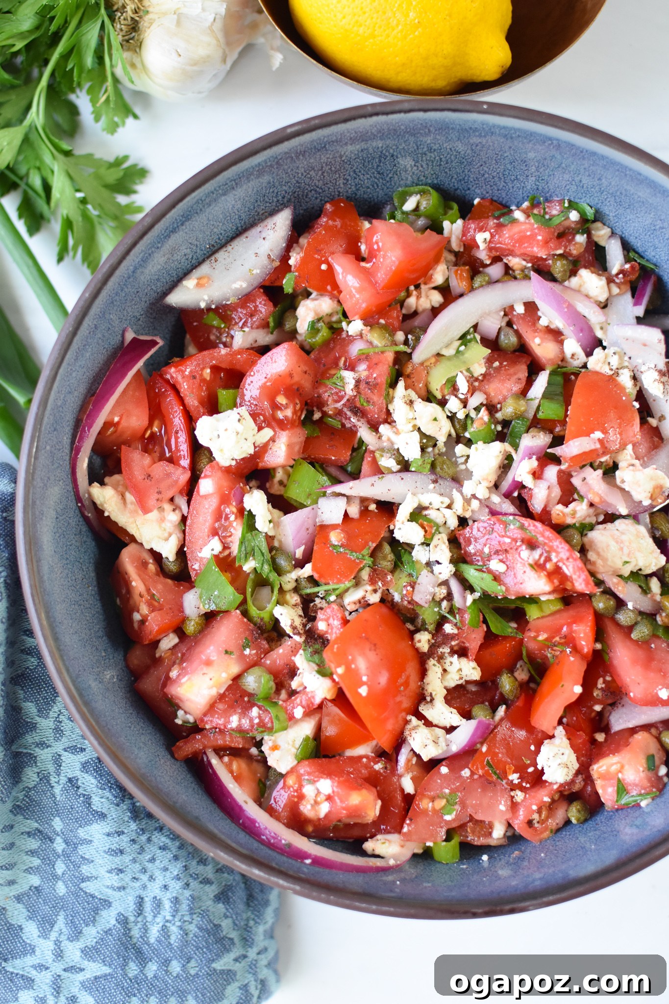 Garden Fresh Tomato Toss 2 Easy Tomato Salad in a blue bowl, showcasing ripe tomatoes, crumbled feta cheese, and fresh green herbs.