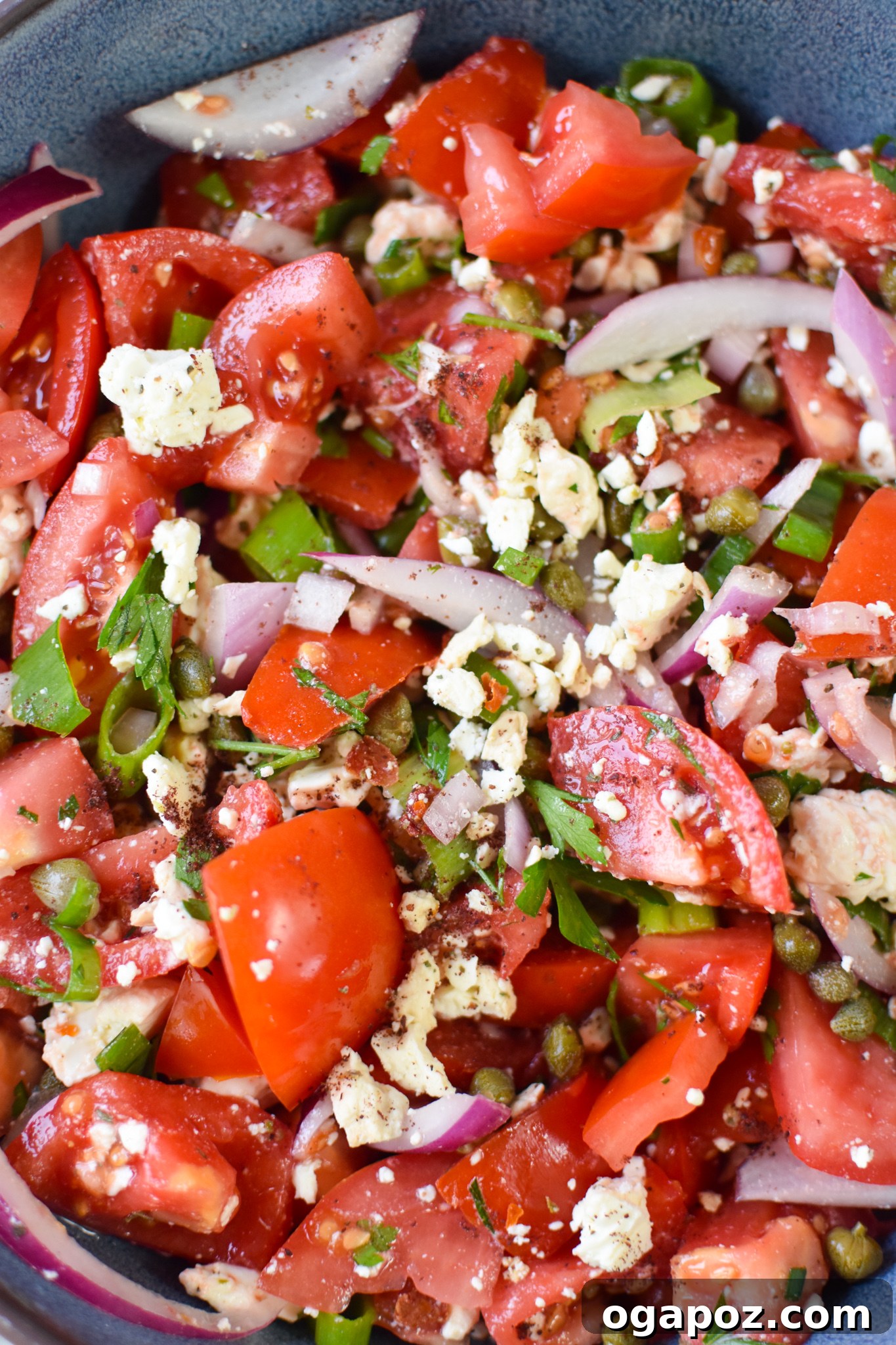 Garden Fresh Tomato Toss 4 Close-up of Easy Tomato Salad served in a blue bowl, highlighting the texture of capers, fresh parsley, and creamy feta cheese.