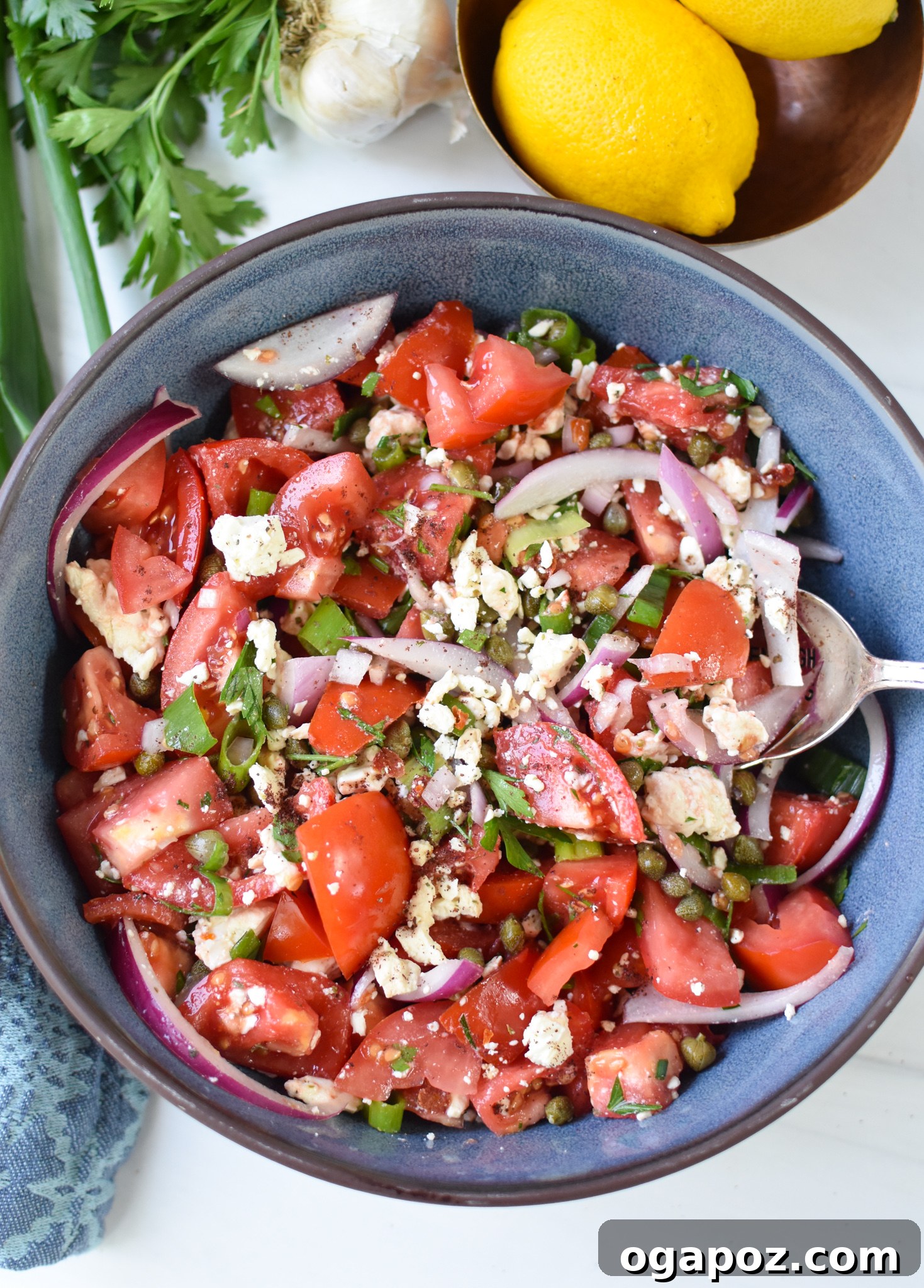 Garden Fresh Tomato Toss 6 Easy Tomato Salad served in a blue bowl with a serving spoon, garnished with fresh herbs.