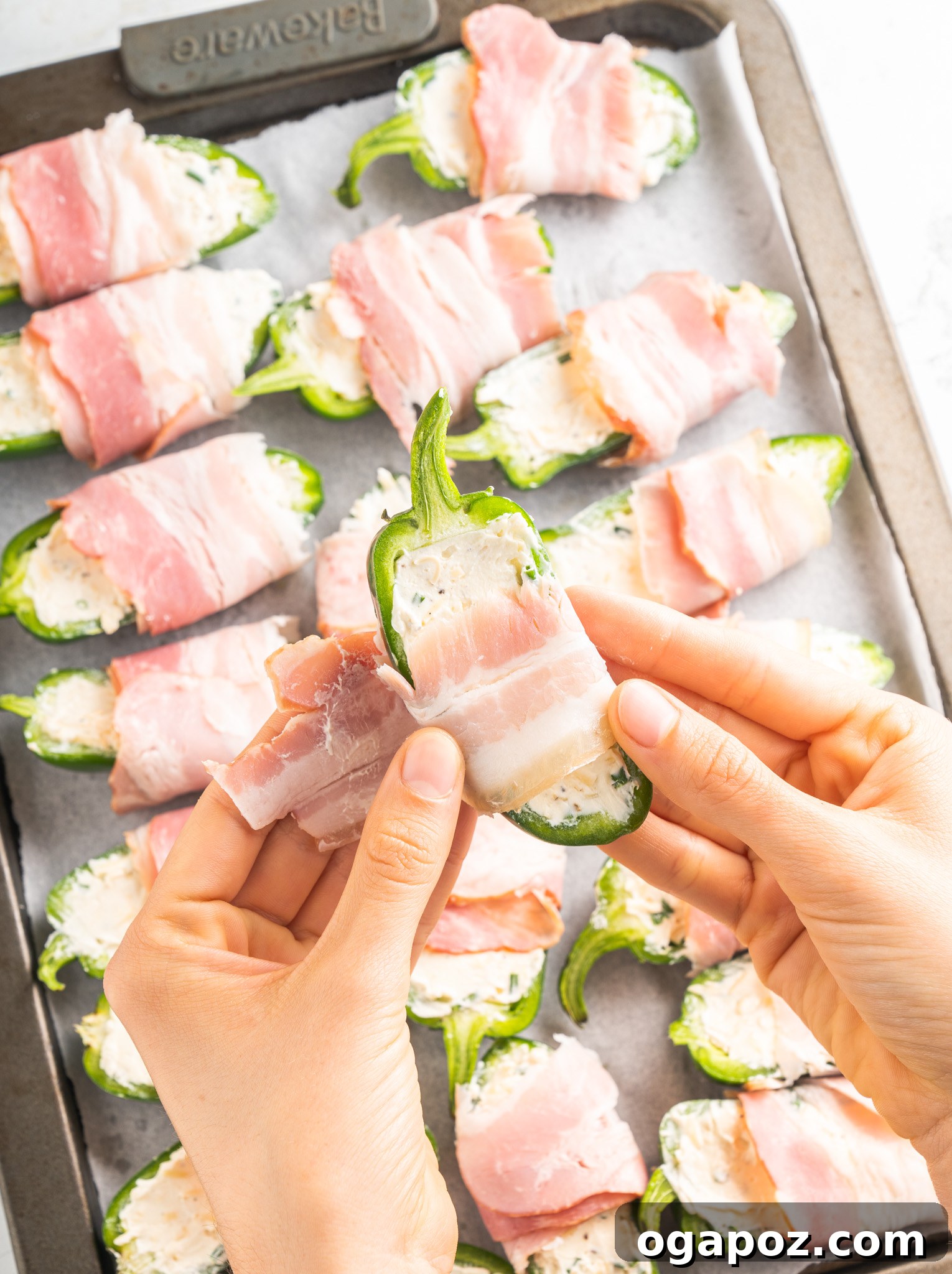 Bacon-Wrapped Jalapeño Bombs 8 Jalapeño poppers being wrapped with slices of bacon on a cutting board.