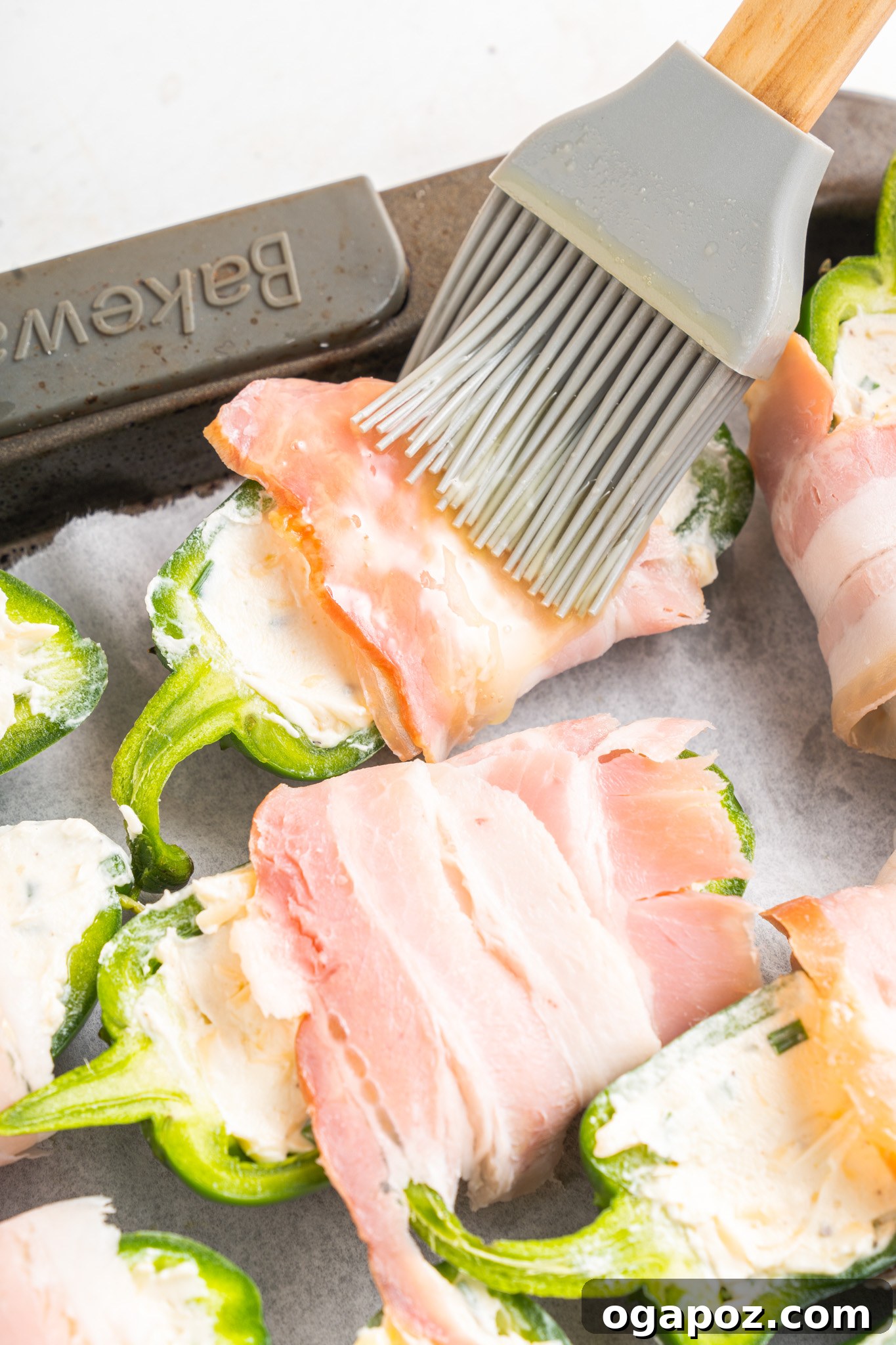 Bacon-Wrapped Jalapeño Bombs 9 Brushing the bacon-wrapped jalapeño poppers with a honey-butter glaze on a baking sheet.