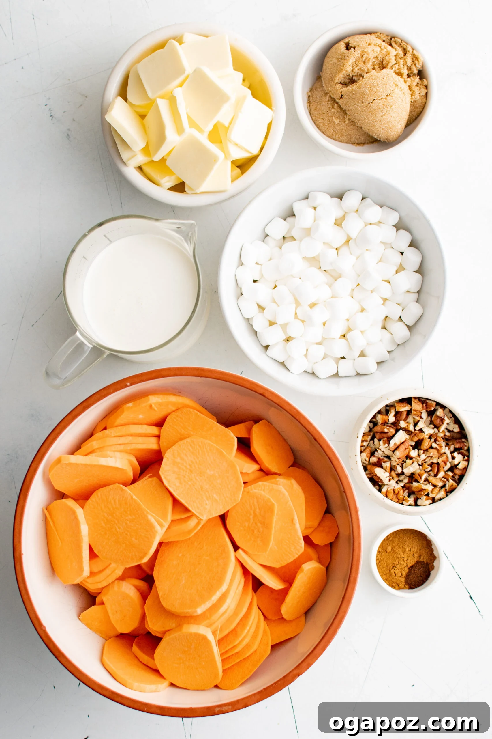 Simple Golden Sweet Potato Gratin 5 A flat lay photograph showcasing all the ingredients for scalloped sweet potatoes: thinly sliced sweet potatoes, marshmallows, heavy cream, cubes of butter, chopped pecans, and a bowl of brown sugar.