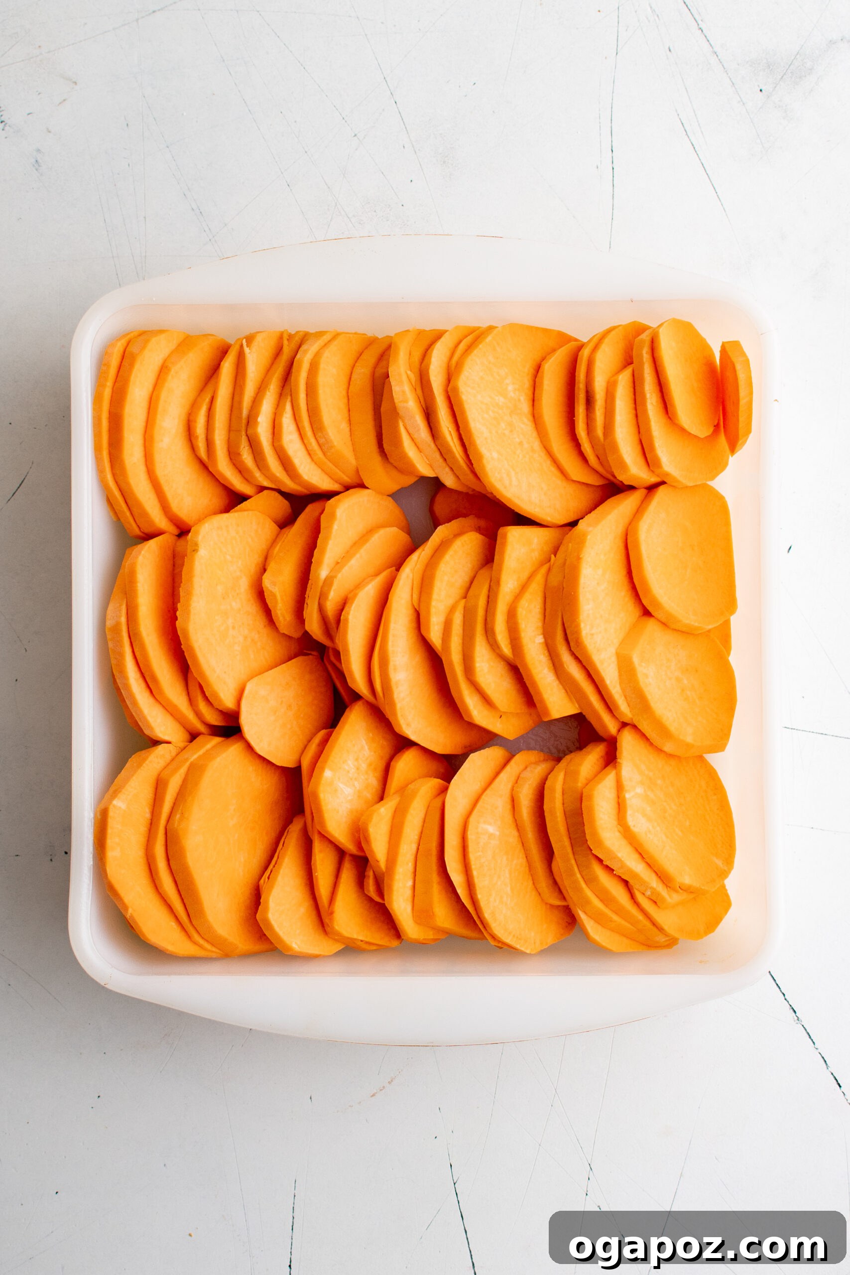 Simple Golden Sweet Potato Gratin 6 Thinly sliced sweet potatoes meticulously arranged in overlapping layers within a baking dish, ready for seasoning and cream.