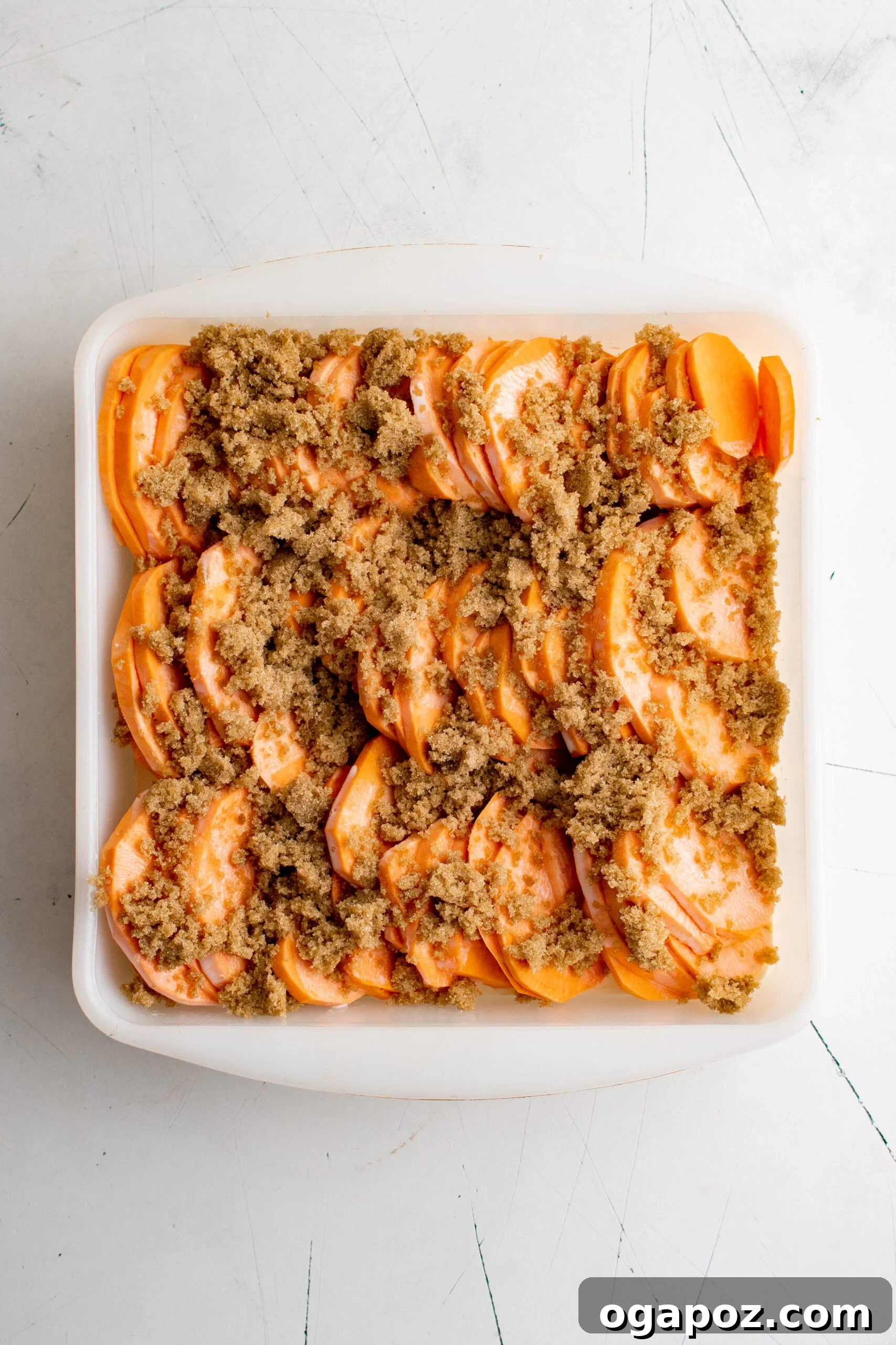 Simple Golden Sweet Potato Gratin 7 Scalloped sweet potatoes in a baking dish, with heavy cream drizzled over, and brown sugar and butter slices distributed on top of the layers.