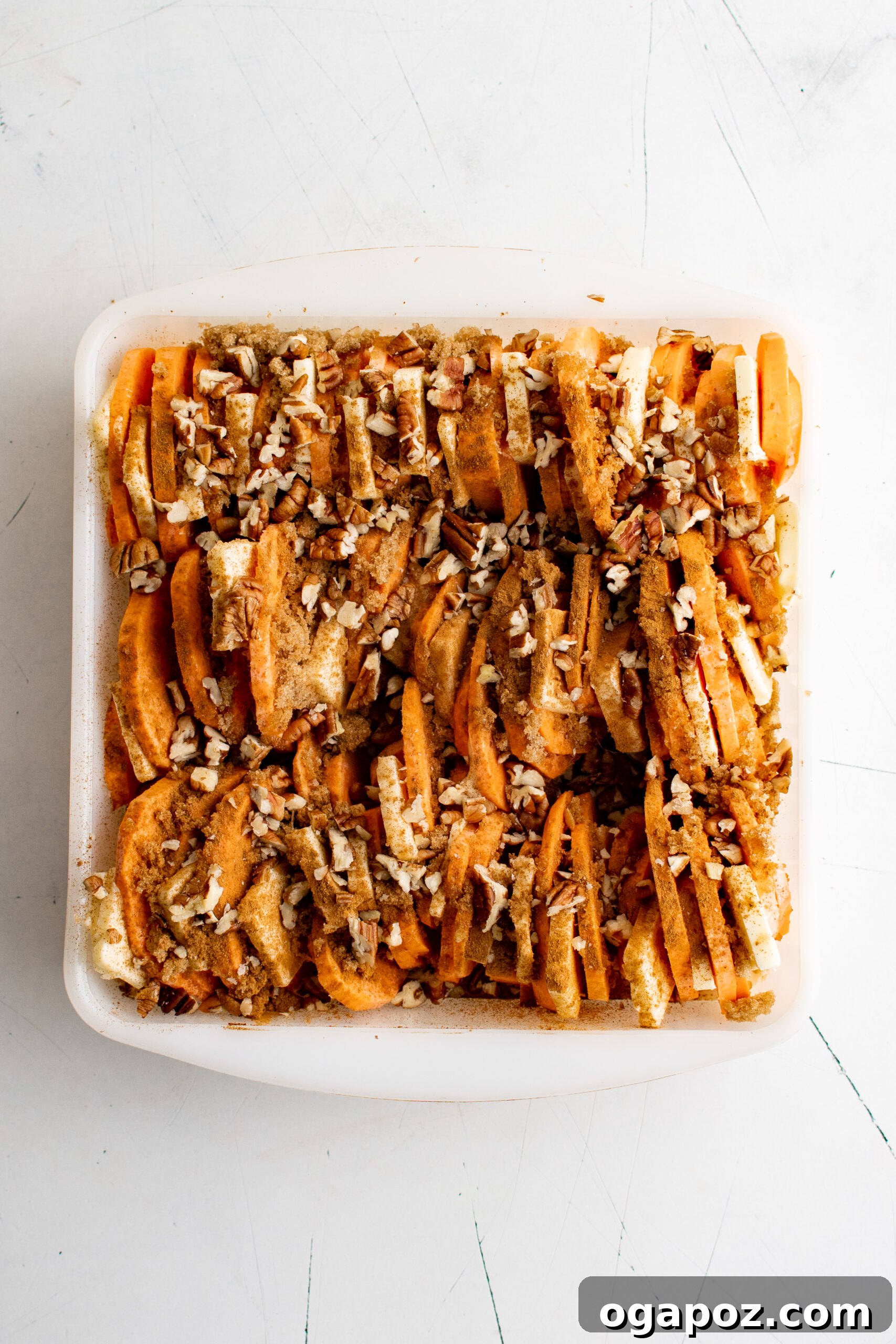 Simple Golden Sweet Potato Gratin 8 Sweet potatoes in a baking dish, now sprinkled with cinnamon, cloves, and a generous layer of chopped pecans over the brown sugar and butter.