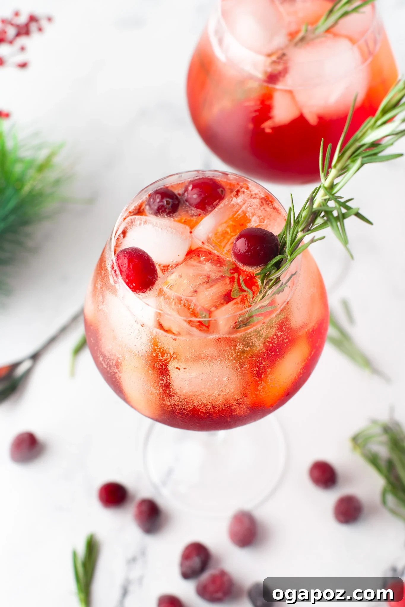 Two glasses of Cranberry Aperol Spritz garnished with fresh cranberries and rosemary, perfect for winter holidays.