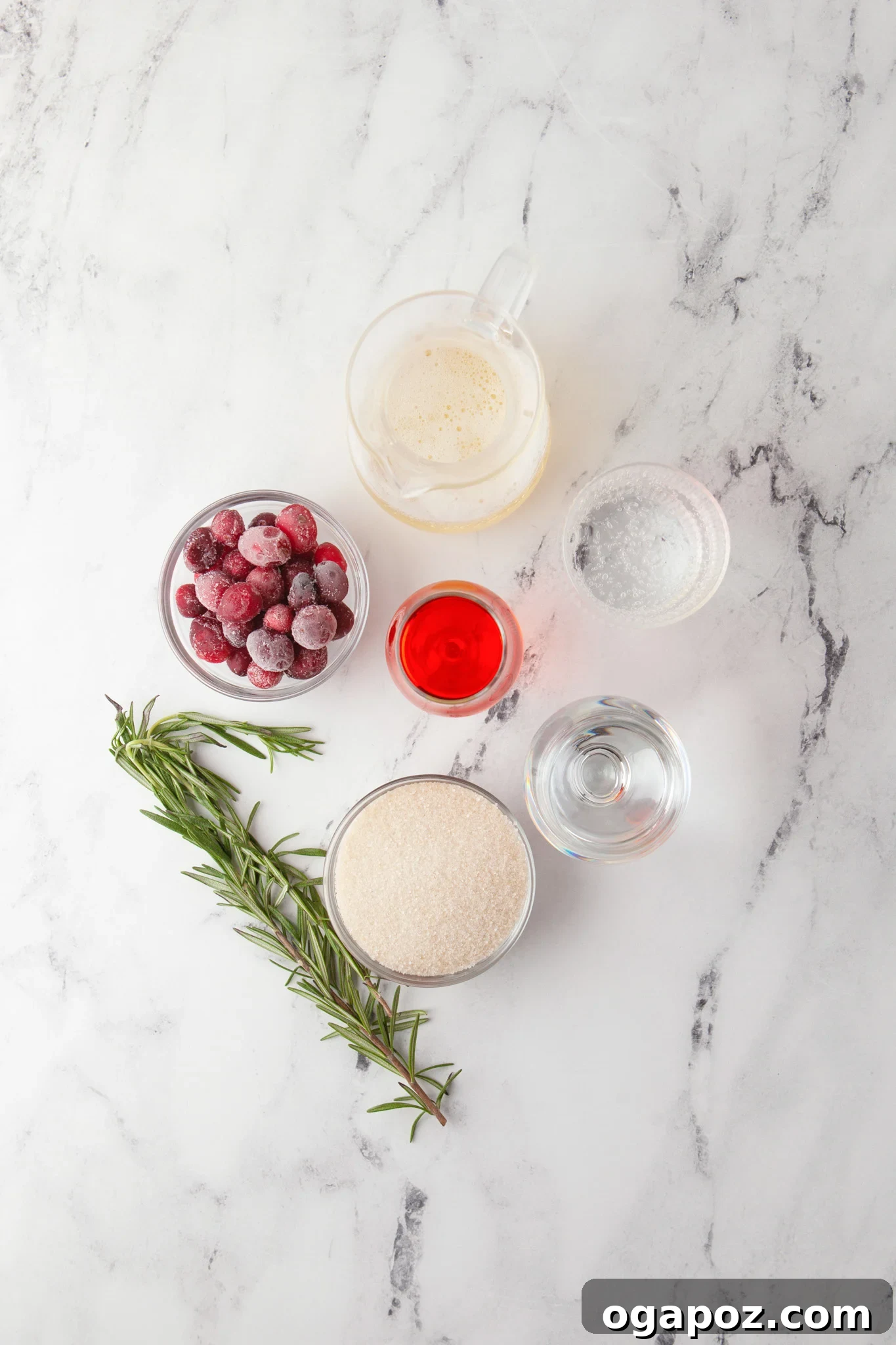 Fresh cranberries, Aperol, Prosecco, soda water, and rosemary sprigs laid out as ingredients for Cranberry Aperol Spritz.
