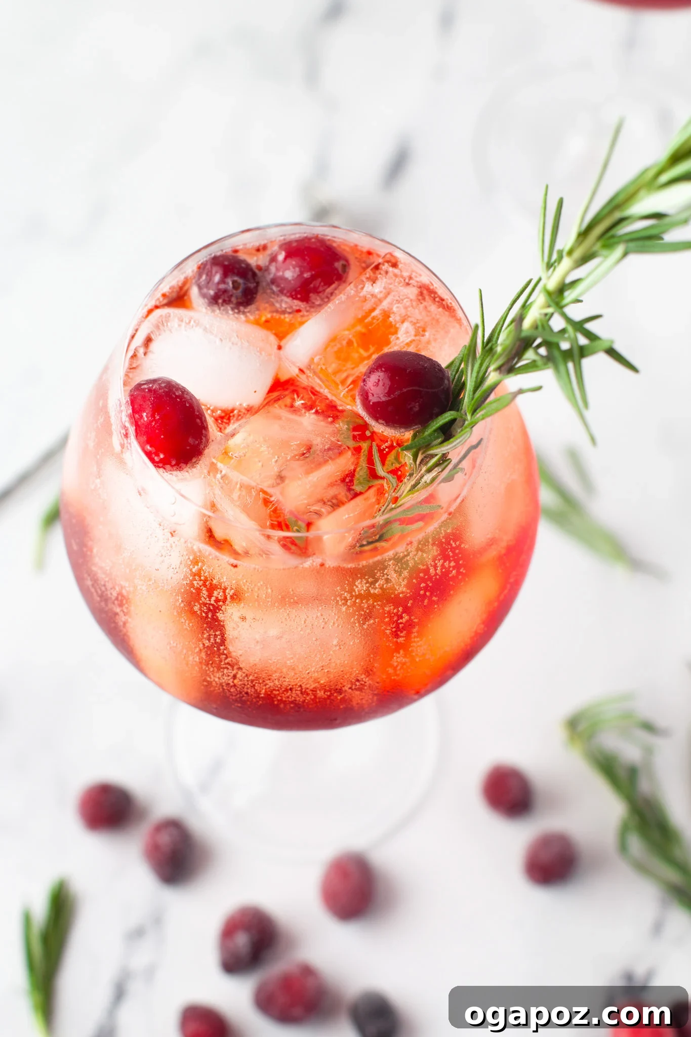 A festive Cranberry Aperol Spritz in a glass, adorned with fresh cranberries and a sprig of rosemary.