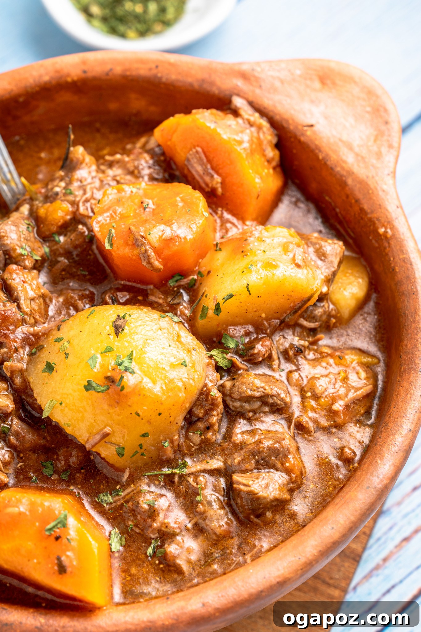 Crock Pot Beef Stew in a warm brown bowl, garnished with fresh herbs.