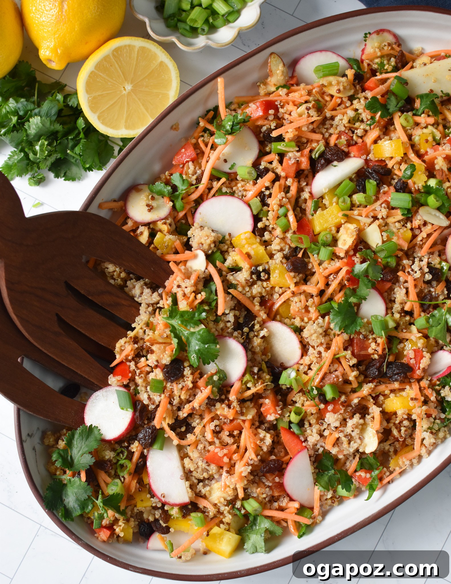 Curried Quinoa Salad served in a large wooden bowl with wooden tongs, showcasing its vibrant colors and ingredients like quinoa, carrots, bell peppers, and fresh herbs.