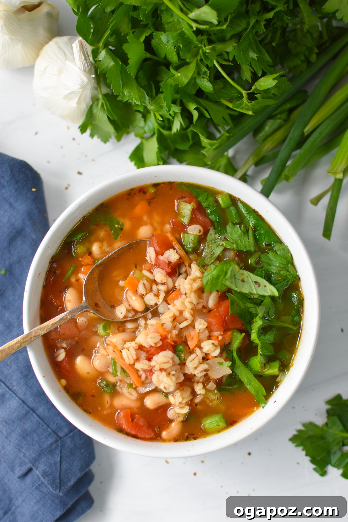 A steaming bowl of hearty Vegetable Barley Soup, garnished with fresh herbs, alongside a gold spoon.