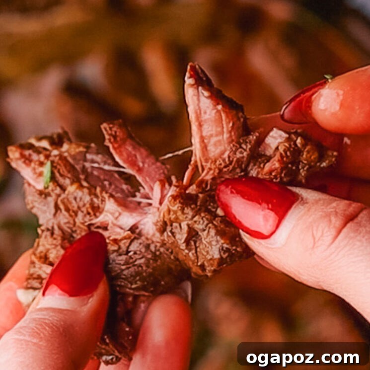 A tender cube of pressure cooker beef stew meat being gently pulled apart with fingers, demonstrating its perfect tenderness.