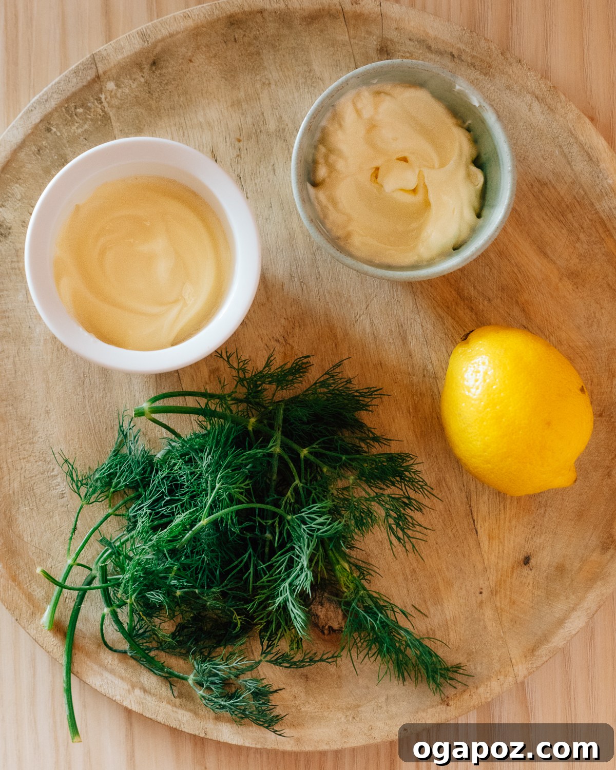 Ingredients for making Dill Sauce for Salmon laid out on a rustic cutting board, including fresh dill, lemon, mayonnaise, and sour cream.