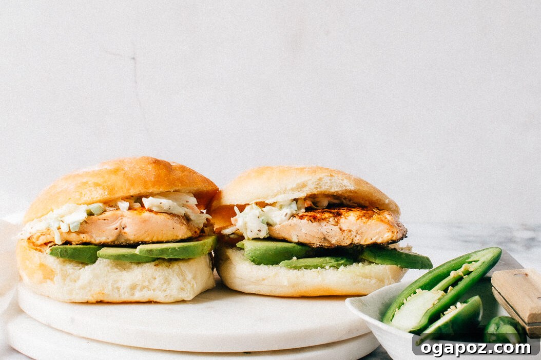 Two salmon burgers served on buns with fresh lettuce, tomato, and generous dollops of creamy dill sauce.