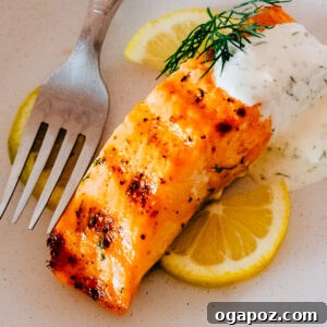 Dill sauce spooned over a filet of salmon on a plate with lemon slices, showcasing a delicious meal.