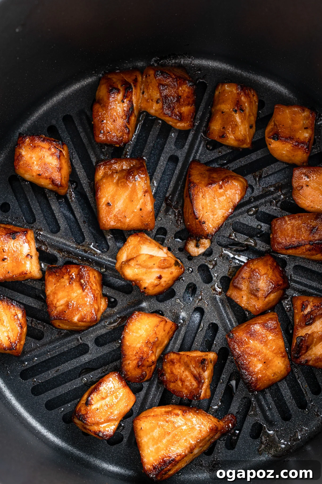 Crispy Air-Fried Teriyaki Salmon Poppers 8 Chunks of glazed salmon are evenly spaced and cooked inside an air fryer basket. The pieces are golden brown with a slight char, indicating they are cooked and ready to eat.