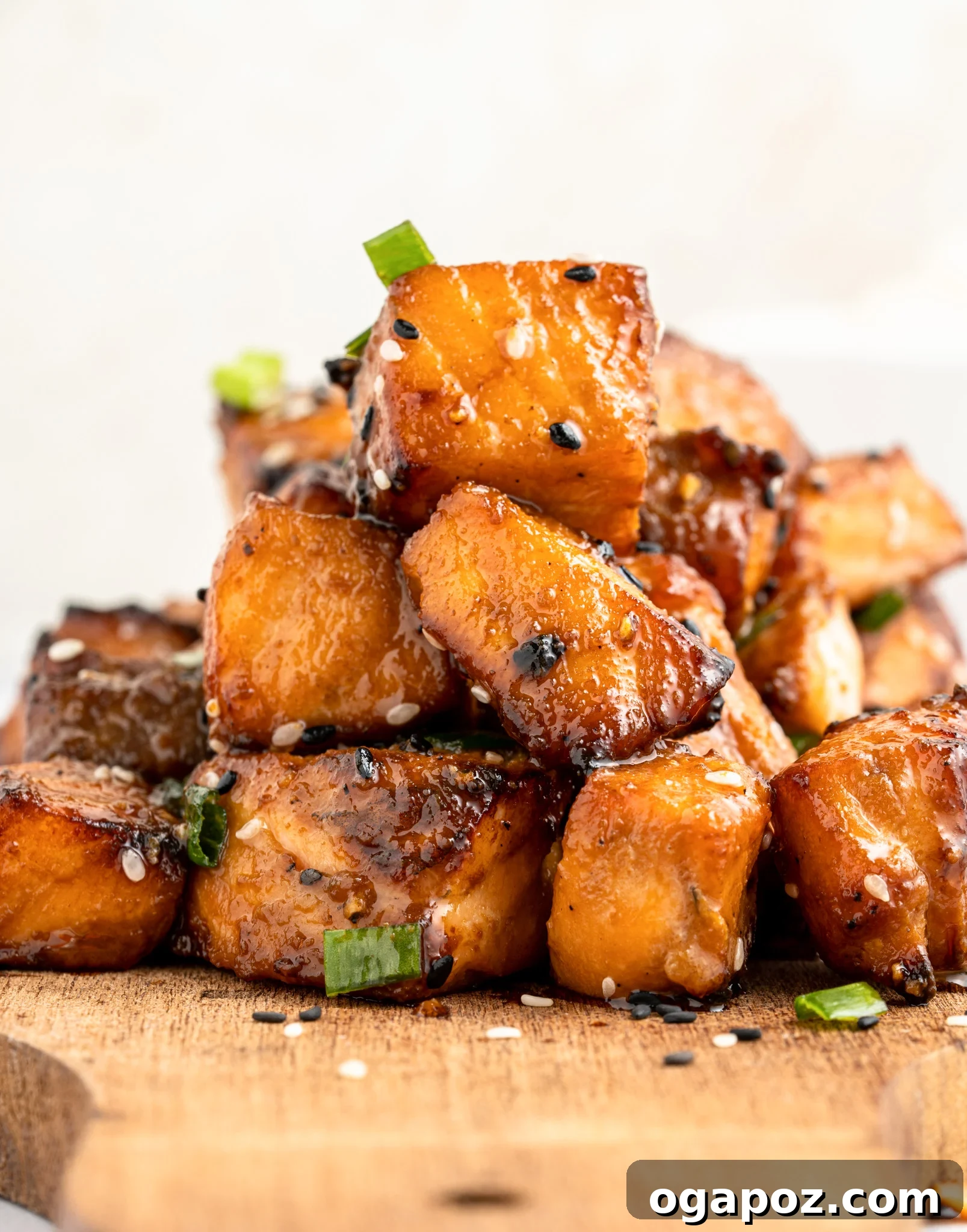 Crispy Air-Fried Teriyaki Salmon Poppers 10 A stack of air fryer salmon bites garnished with sesame seeds and green onions on a wooden board. The pieces are golden-brown, highlighting their caramelized surface.