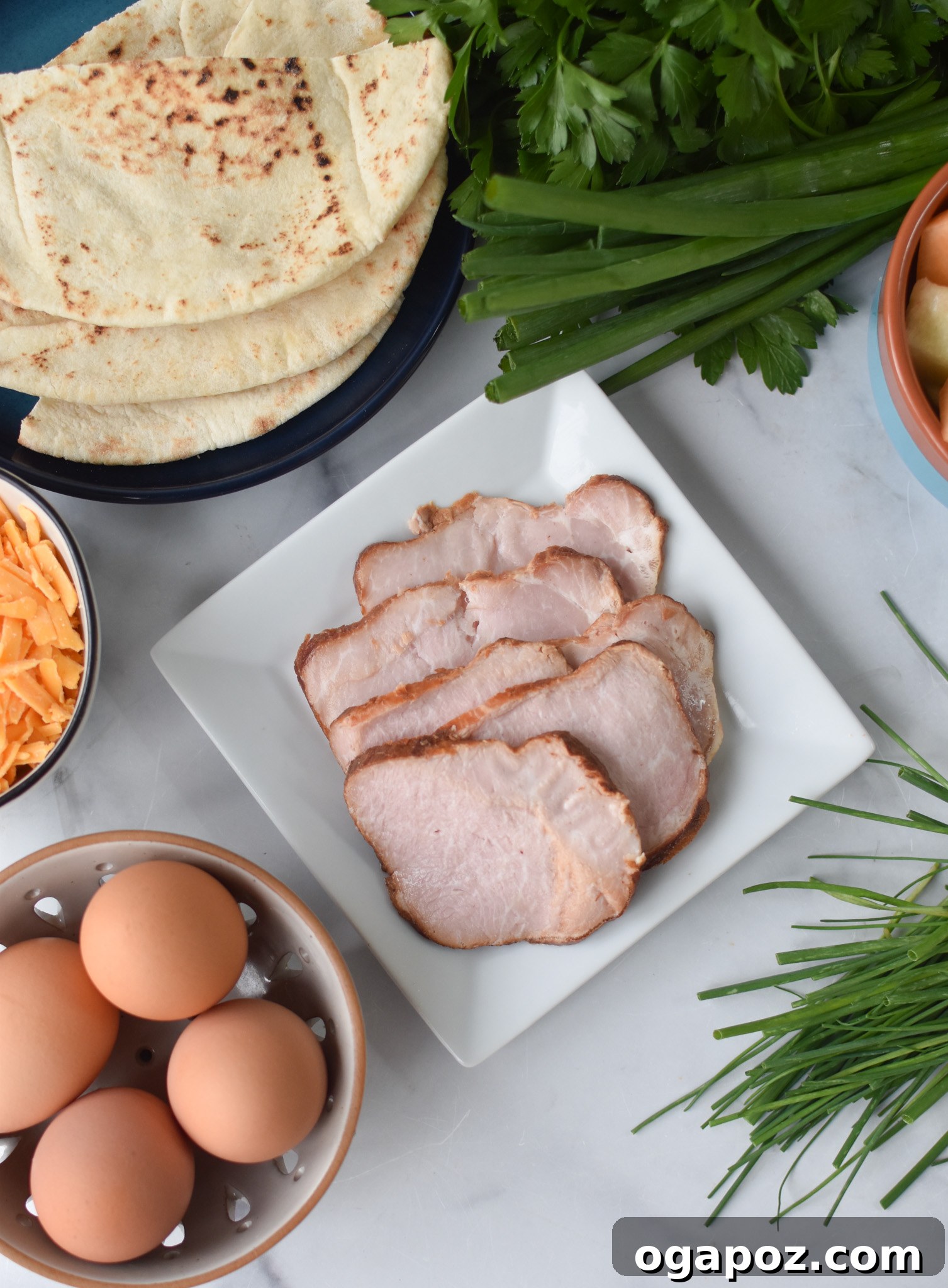 Savory Morning Pitas 3 A colorful array of ingredients for Breakfast Pita, including eggs, bacon, pita bread, chives, and cheddar cheese.